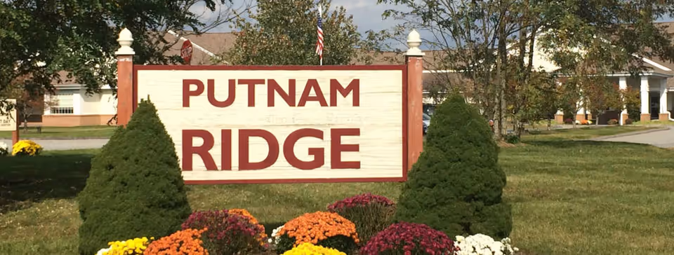 Outdoor Putnam Ridge sign with colorful flowers and trimmed evergreen shrubs.