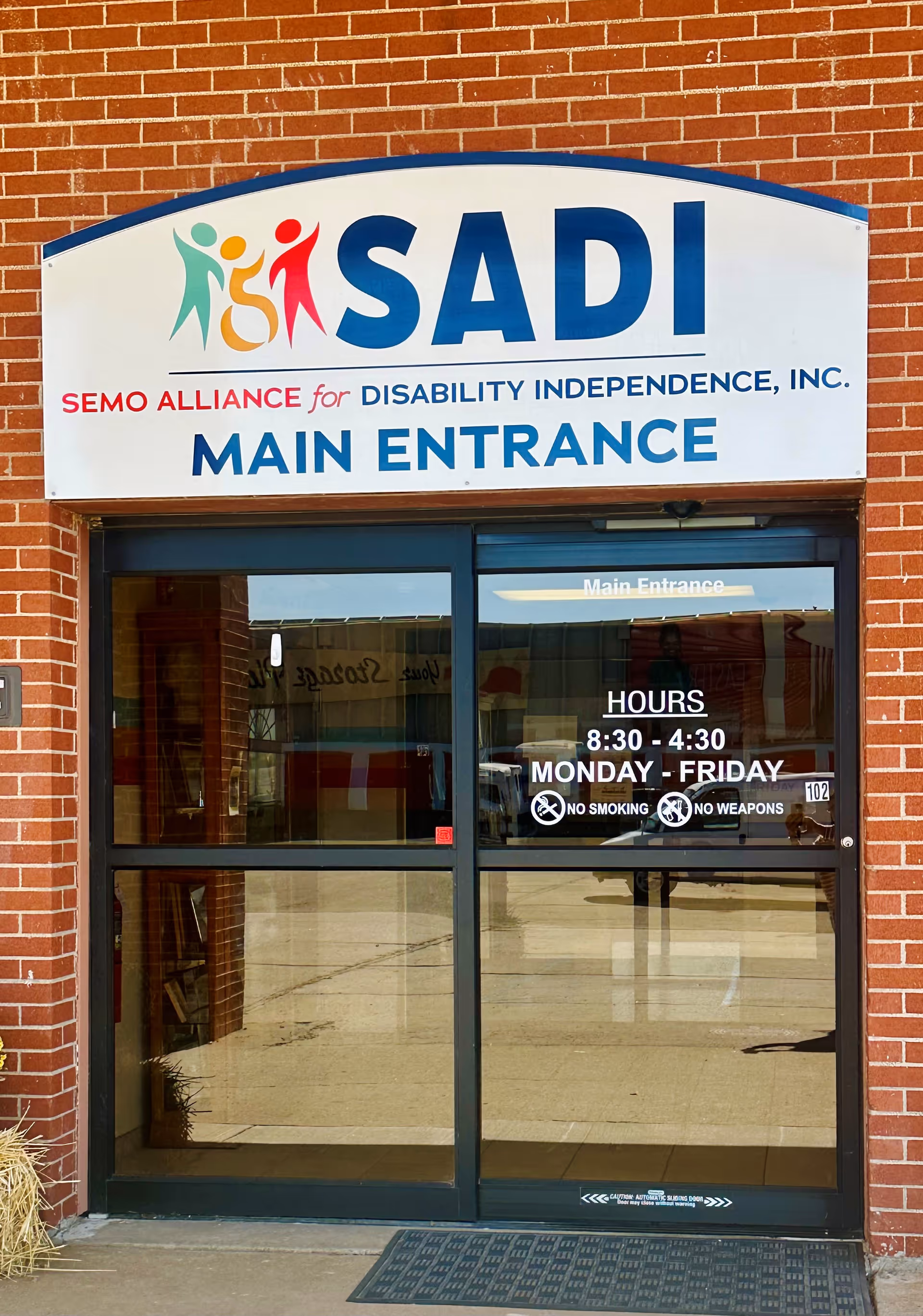 Brick building frontage with a large SADI sign above glass doors labeled Main Entrance.