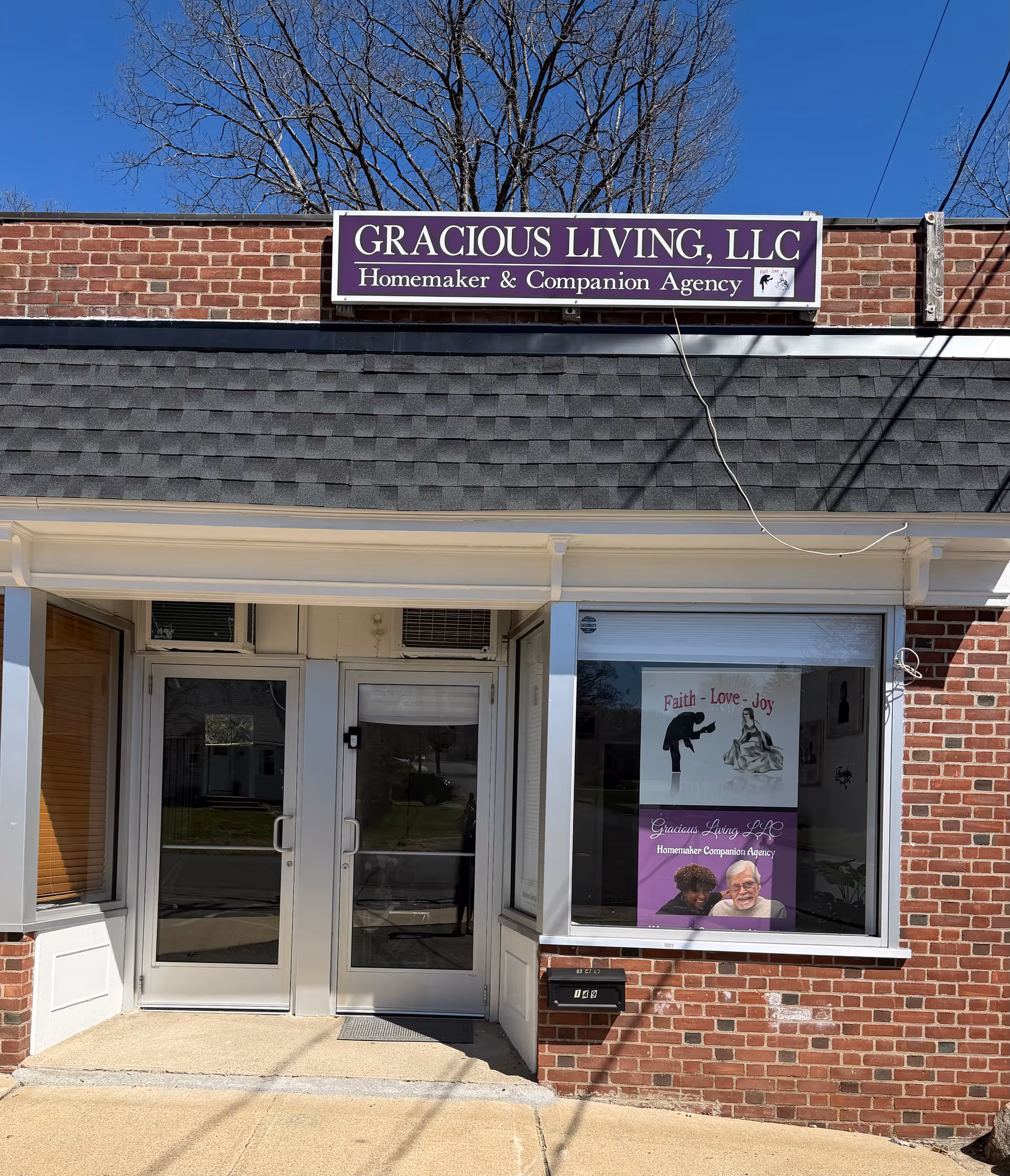 Brick storefront with Gracious Living, LLC sign and glass doors under blue sky.