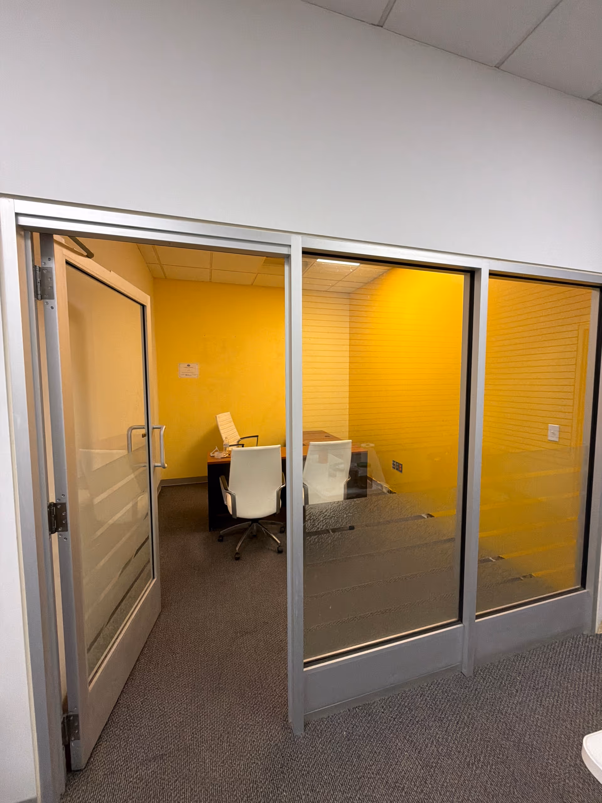 Glass-walled conference room inside a facility with yellow walls and a desk.