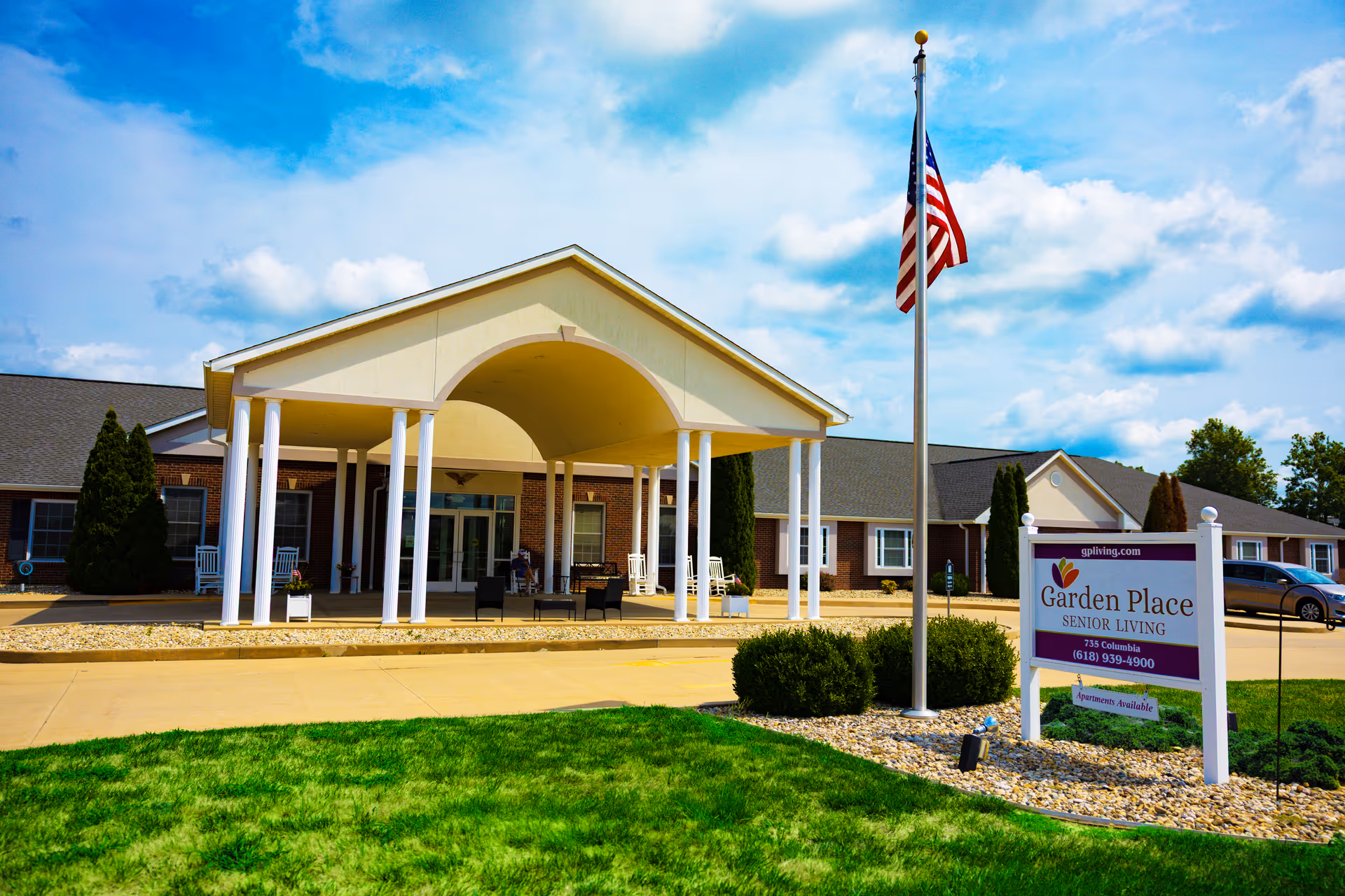 Exterior view of Garden Place Waterloo Senior Living facility with entrance canopy and flagpole