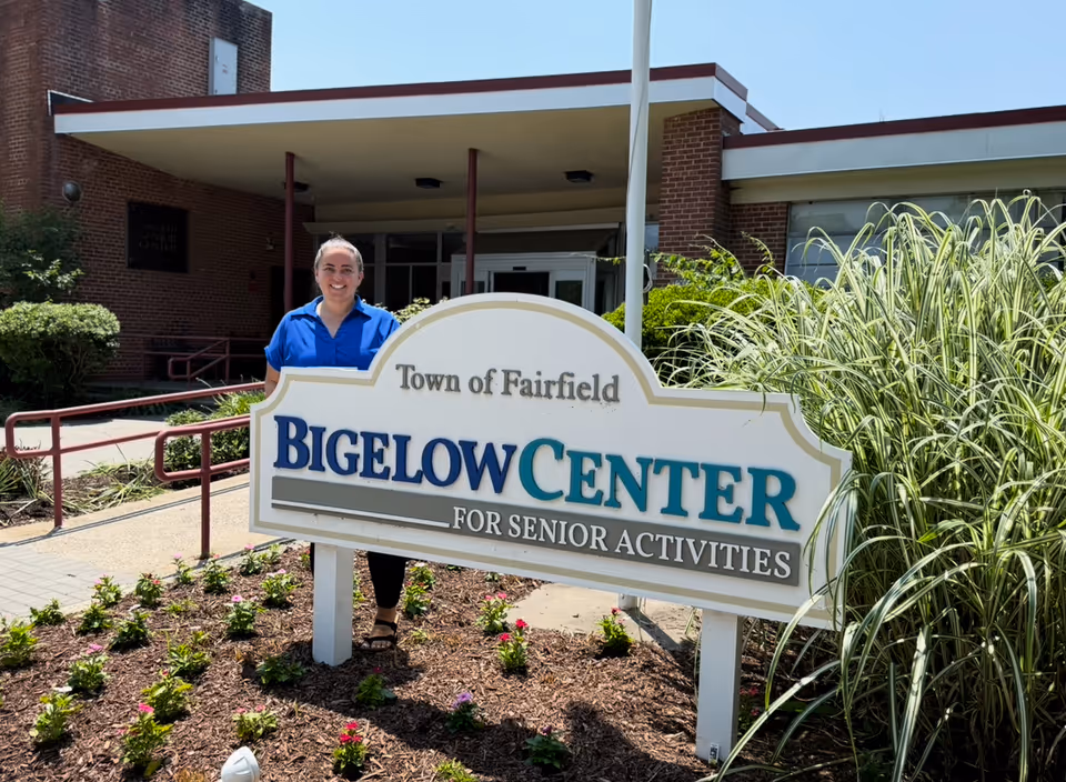 Staff member in blue stands beside the Bigelow Center for Senior Activities sign at the entrance.