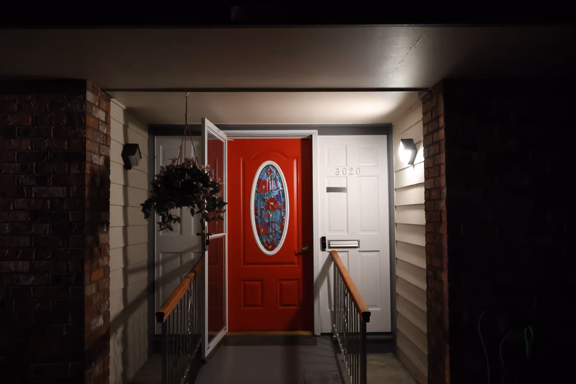 Night exterior of a residence entrance featuring a red door and hanging planter.