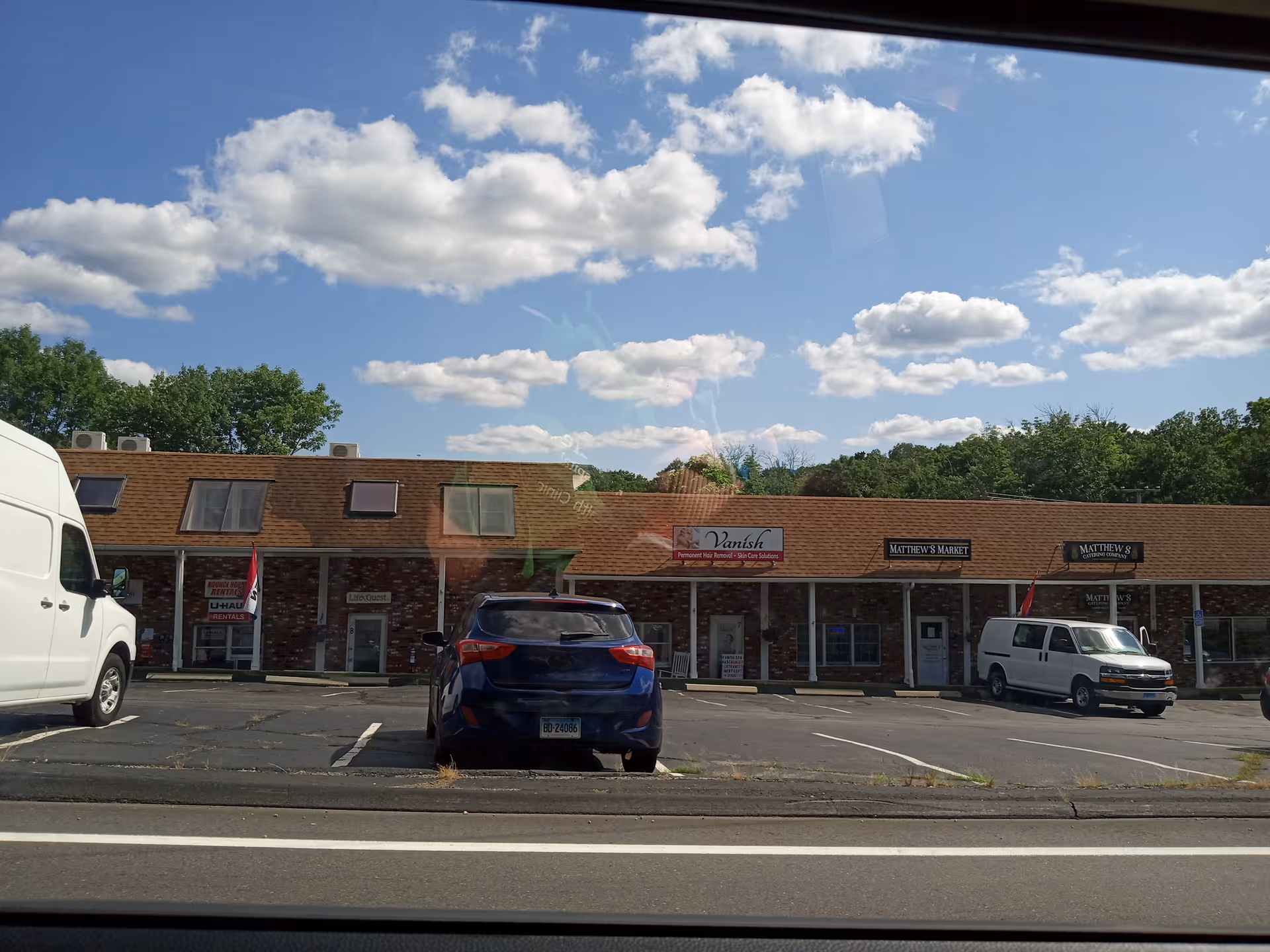 Strip mall storefronts along brick building under blue sky with parked cars in foreground