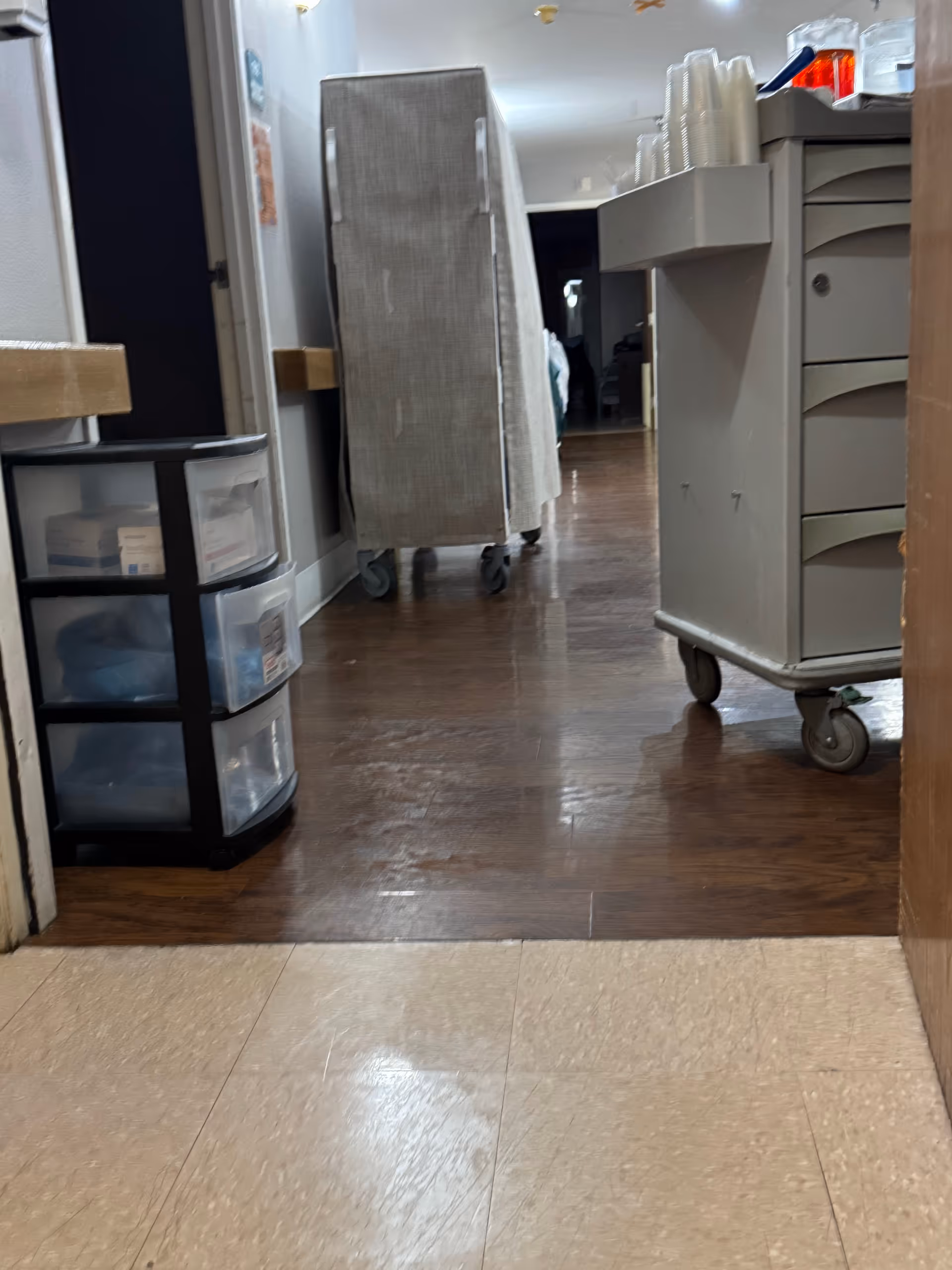 Interior hallway at Cedar Mountain Post Acute with carts, a mattress on wheels, and plastic drawers.