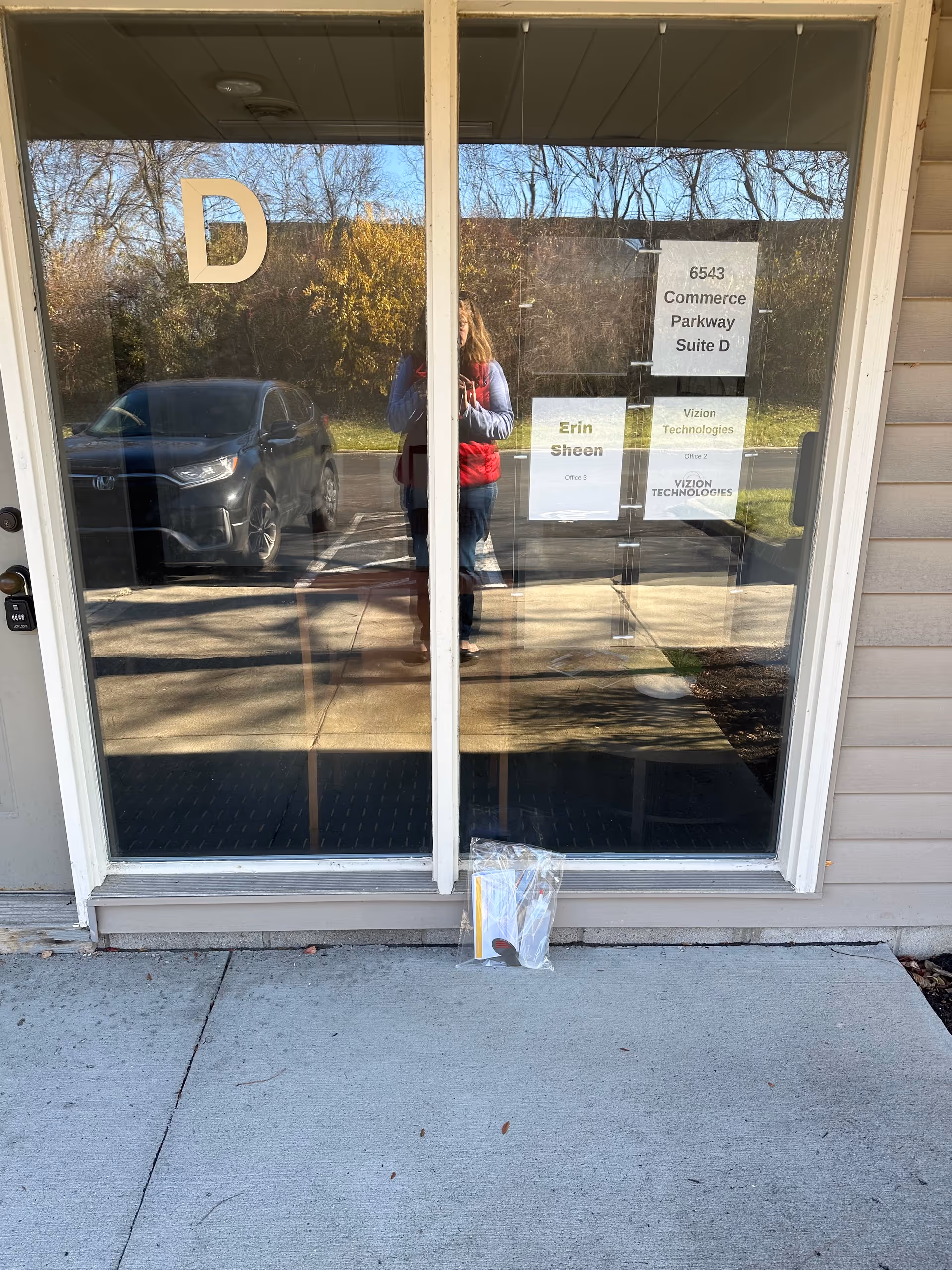 Glass storefront entrance with a large D, door signs, and a reflected person outside.