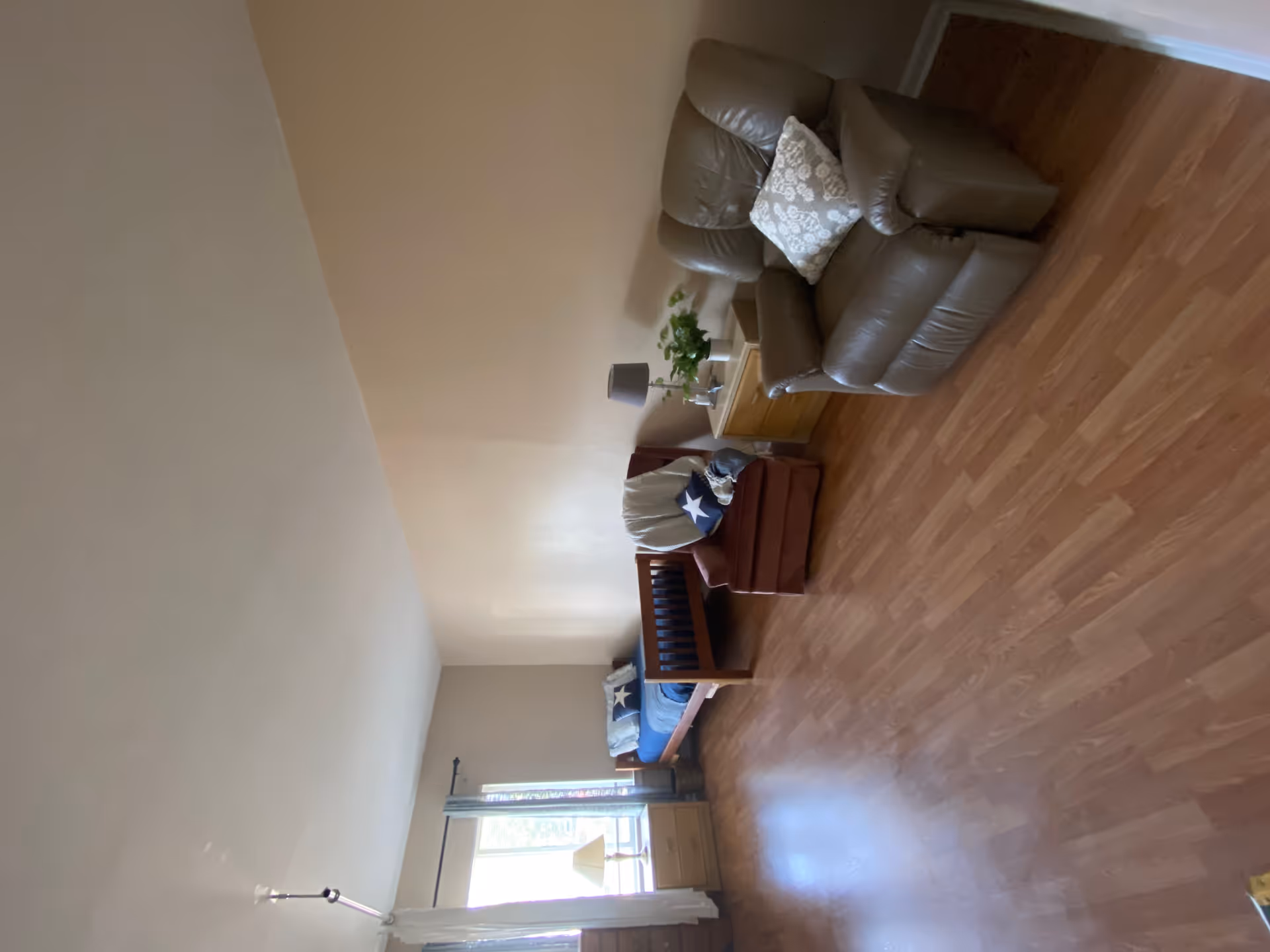 Cozy living room area in a senior facility with leather sofa, armchair, and polished wood floor.