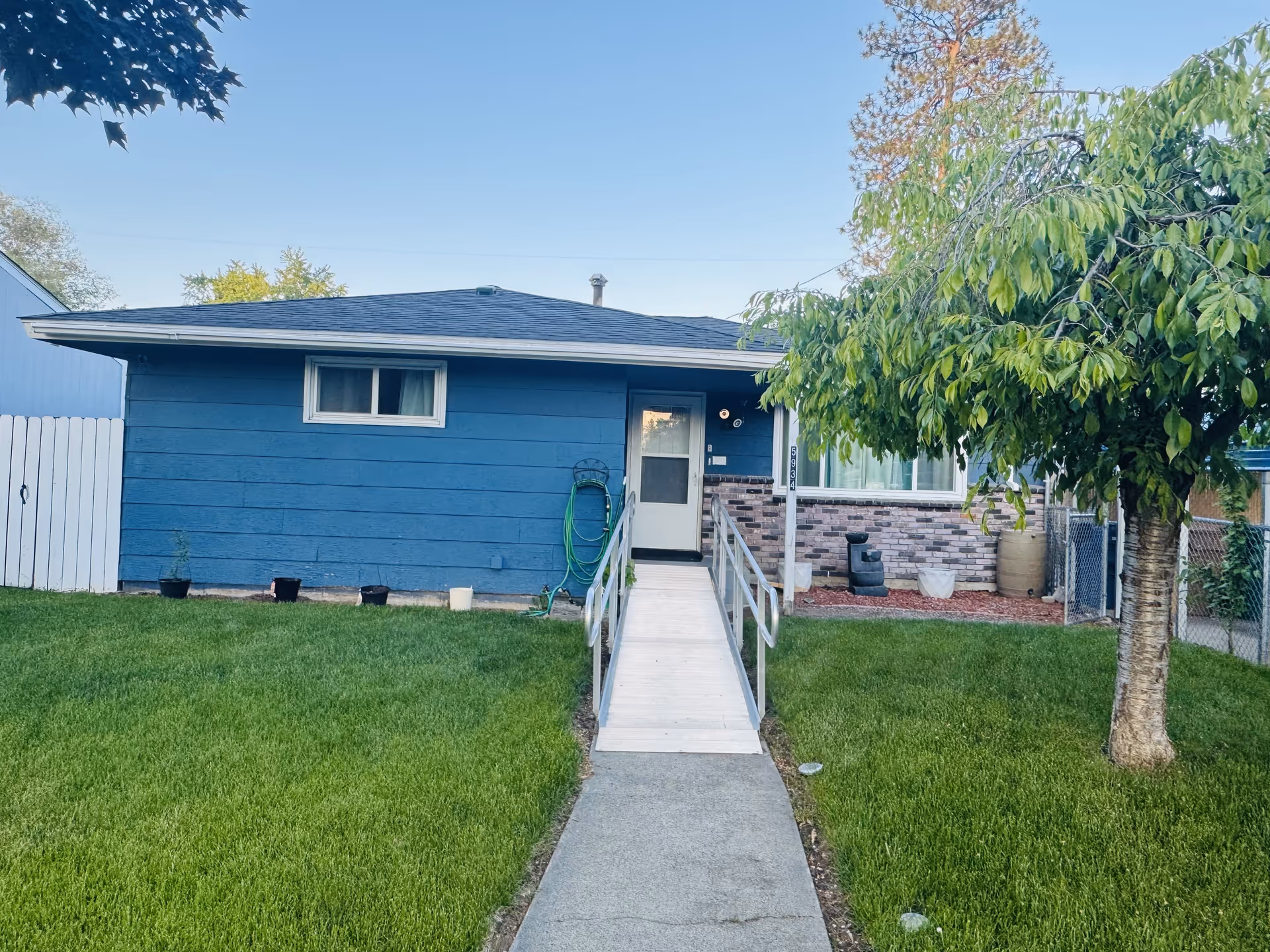 Blue single-story Caringrove Adult Family Home exterior with front ramp, green lawn, and a tree.