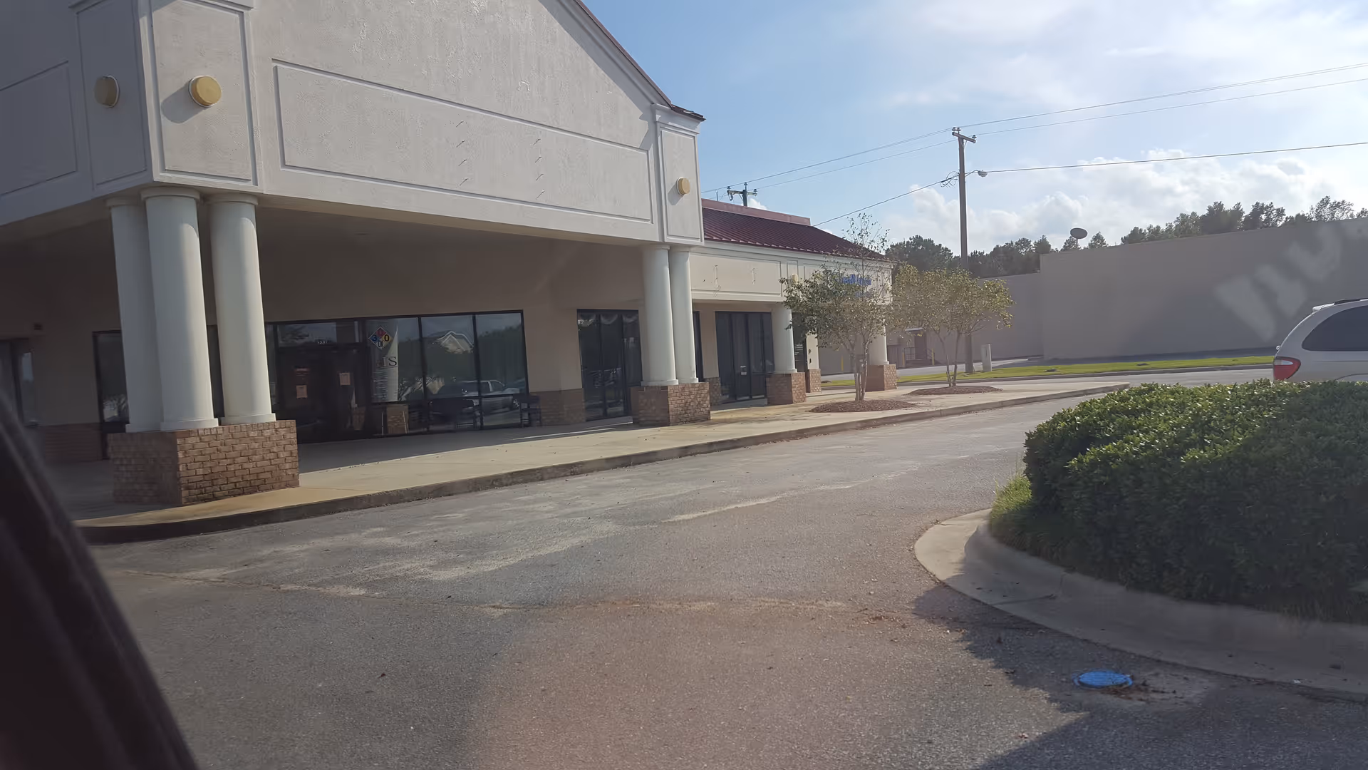 Exterior view of a building with columns, large glass storefronts, and parking.