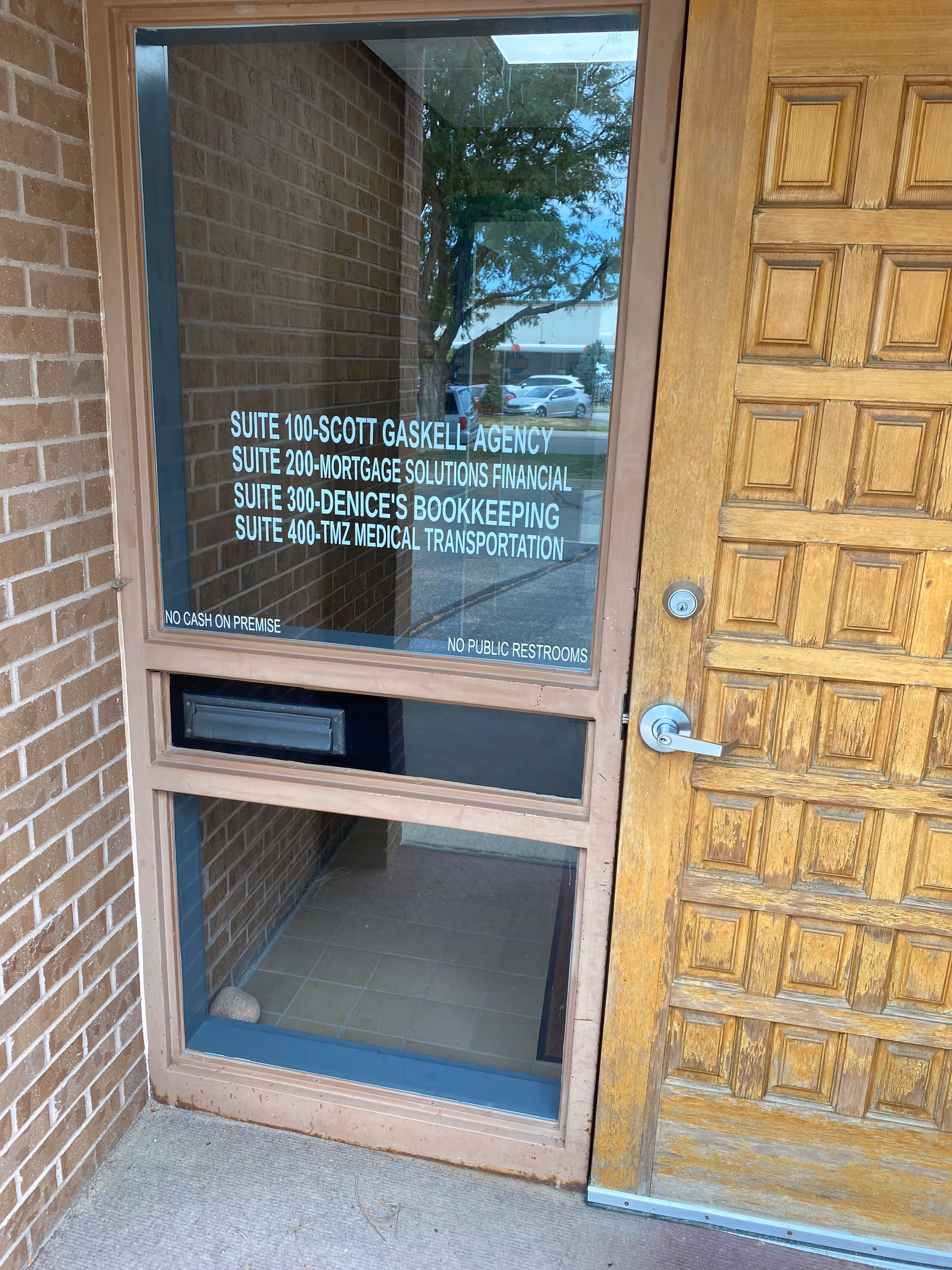 Glass front door with suite listings against a brick exterior and wooden entry door.
