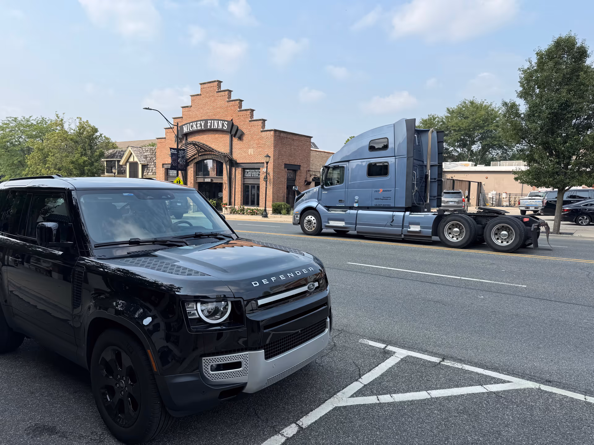 Brick-front building across the street with a blue semi-truck and black SUV in view.