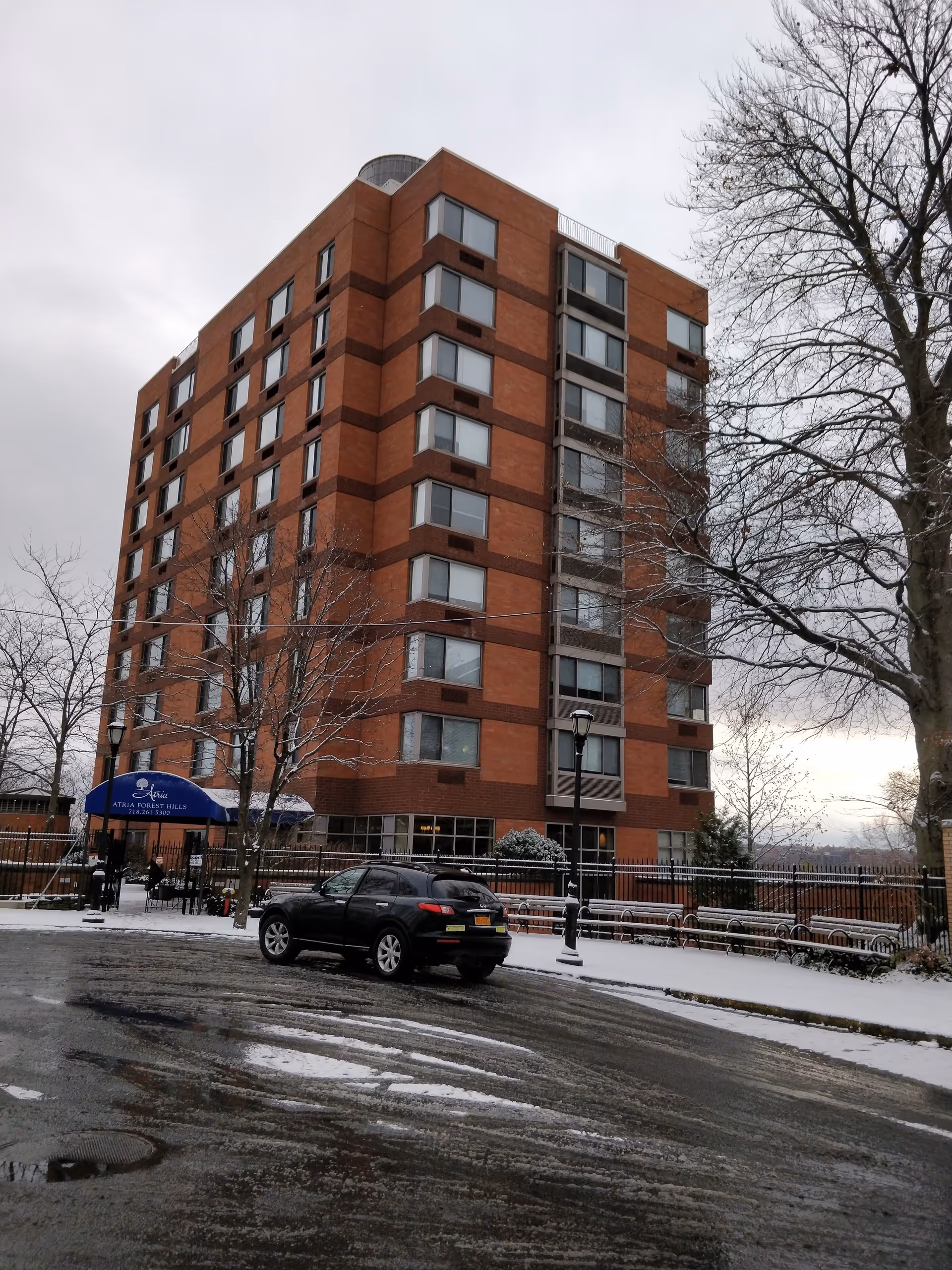 Exterior view of Atria Forest Hills, a tall brick senior living building with snow.