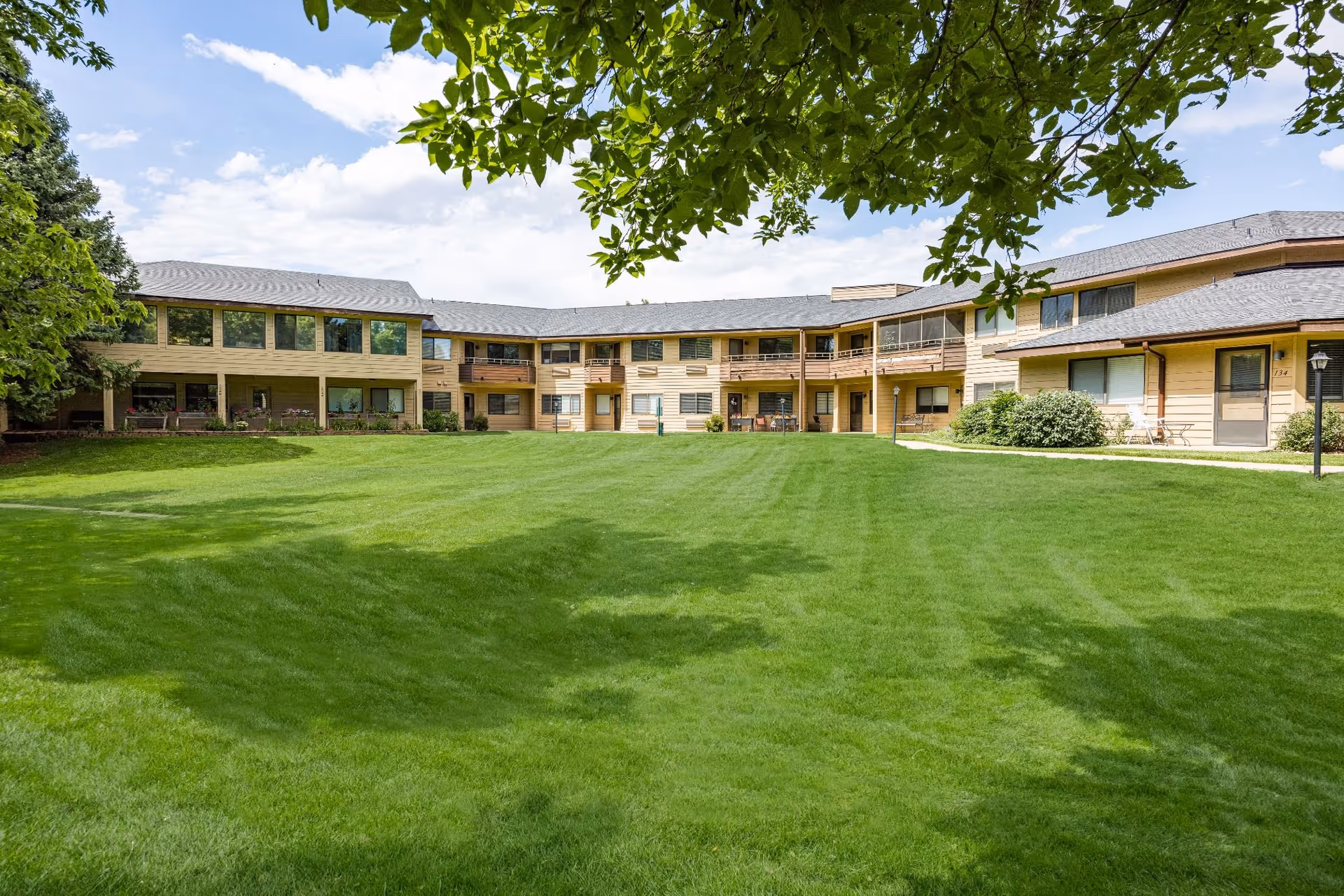 Wide, well-kept lawn borders a beige, two-story senior living building with balconies.