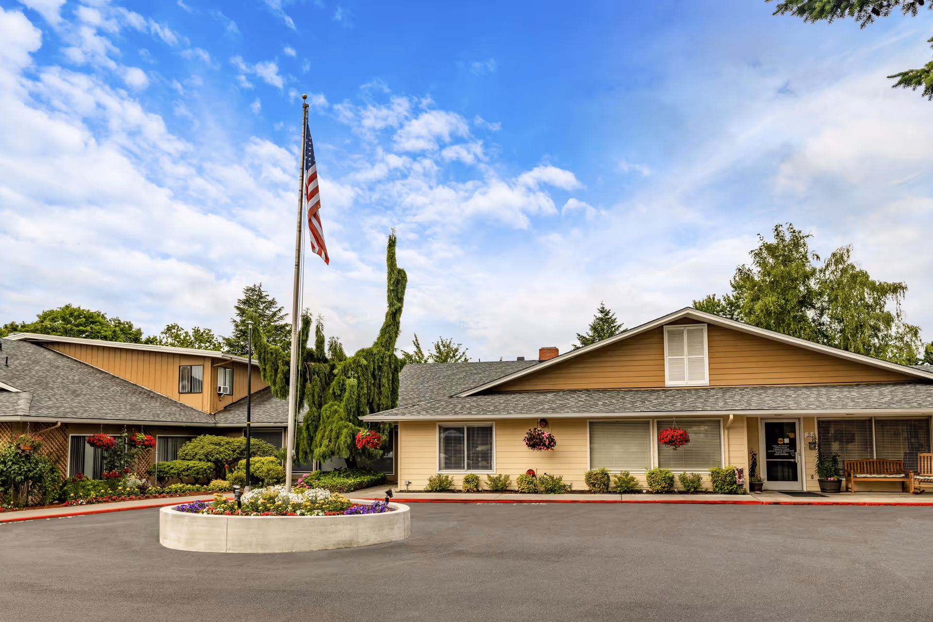 Exterior view of Kamlu Retirement Inn-Vancouver, featuring a flagpole, circular flower bed, and entrance.