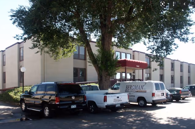 Exterior view of a senior living building with a parking lot and vans.