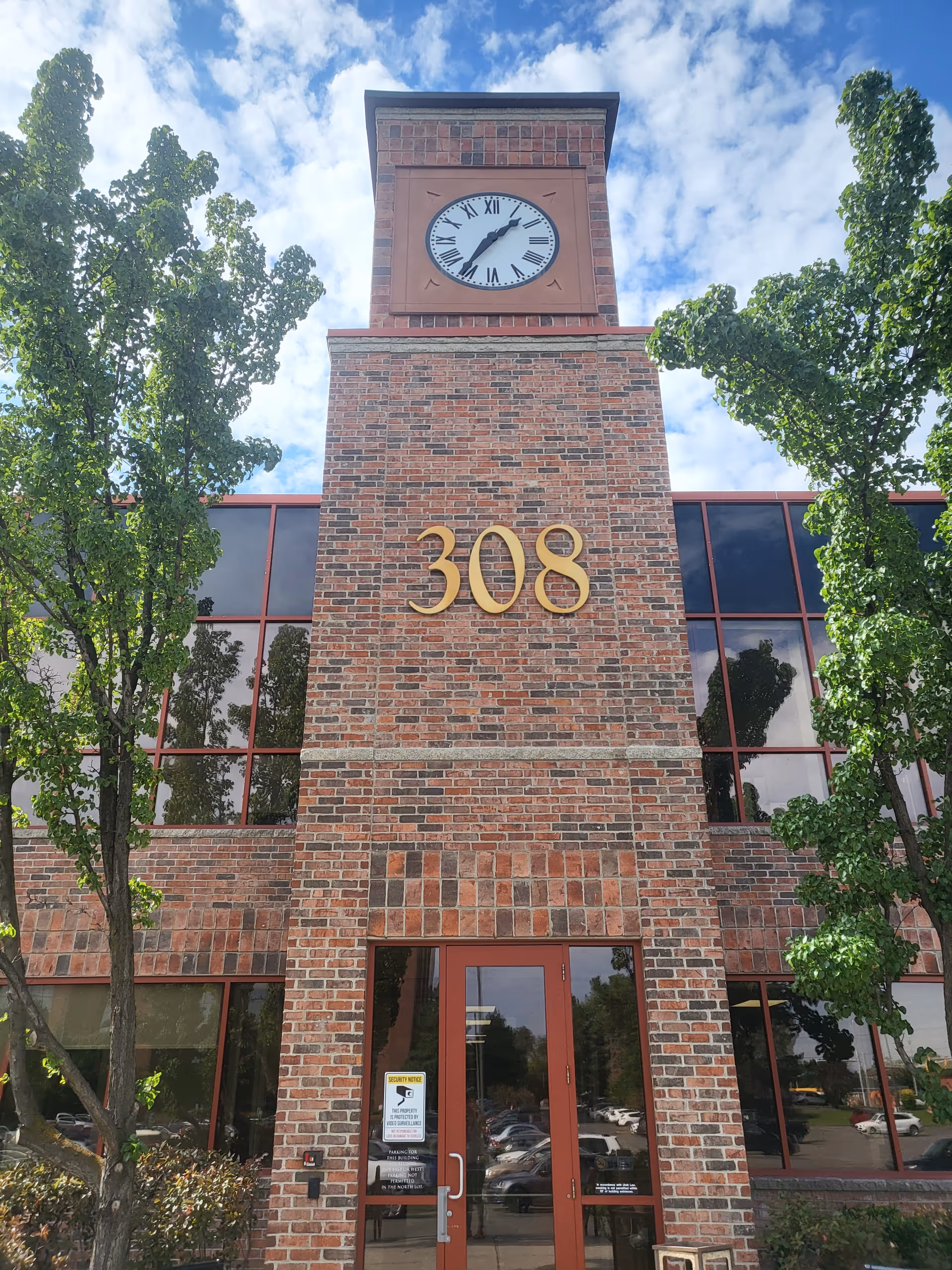 Brick building exterior with clock tower, large 308 numerals, glass windows, and trees.
