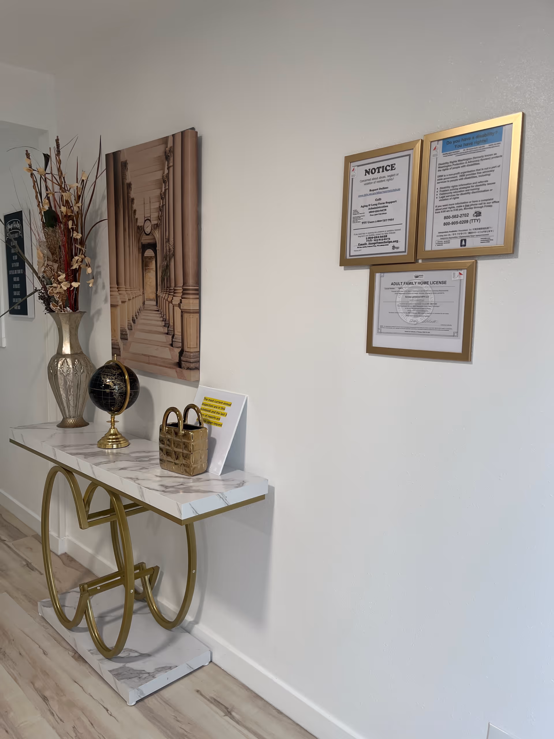 Interior hallway with marble console table, gold legs, decorative vase, globe, and framed notices.