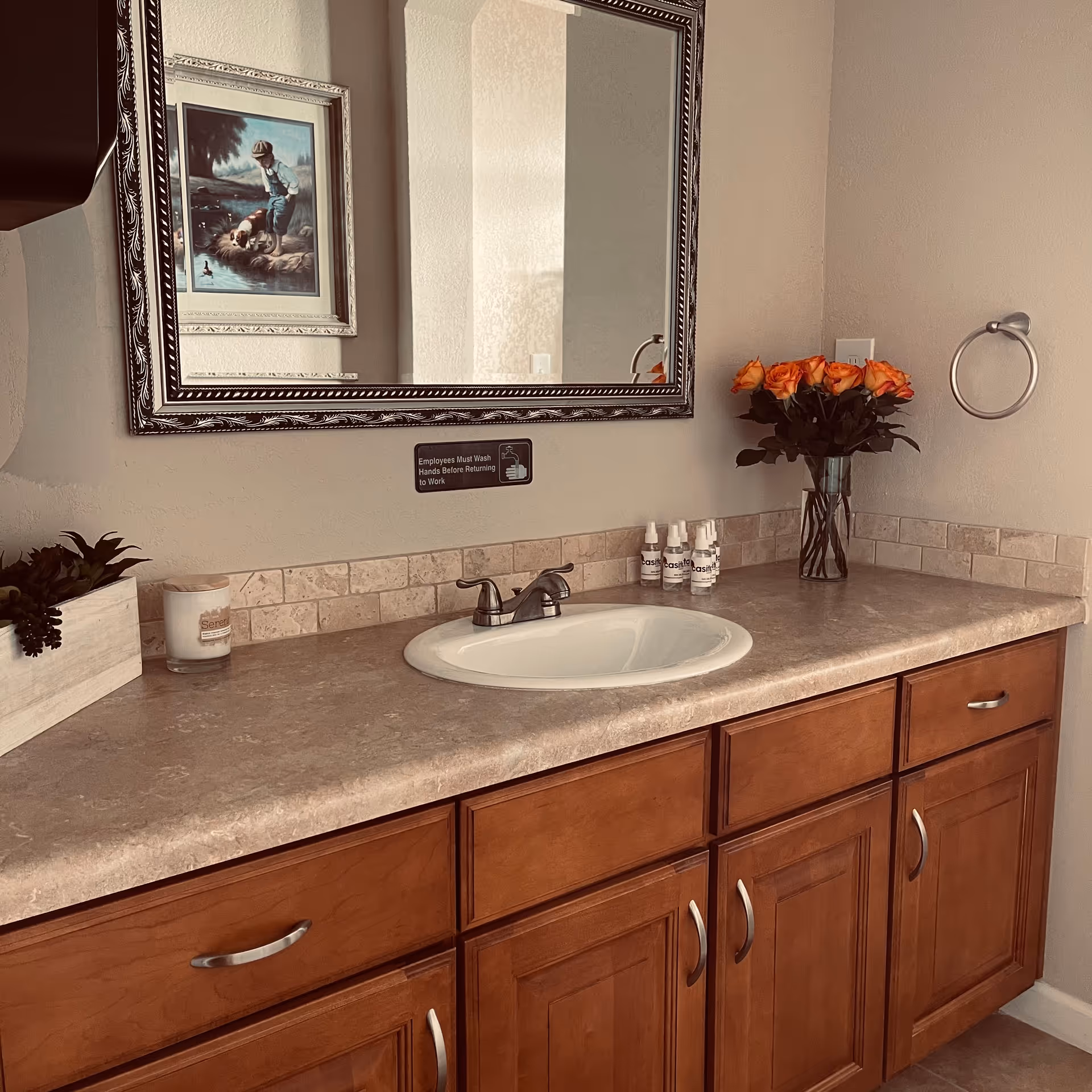Bathroom vanity with sink, mirror, countertop decor, and a vase of orange roses.