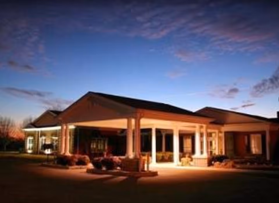 Illuminated covered front entrance of a single-story senior living facility at dusk.