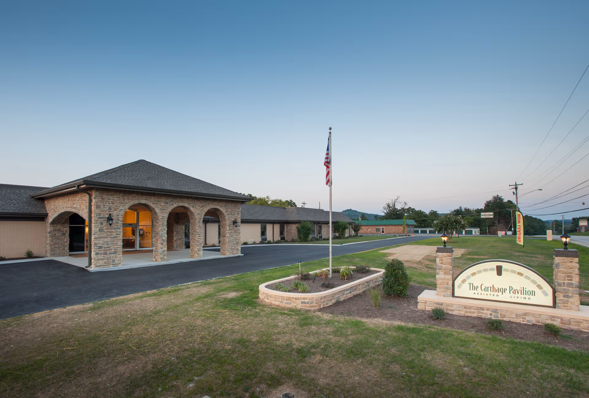 Exterior view of The Pavilion Senior Living Carthage entrance with a flagpole and sign.