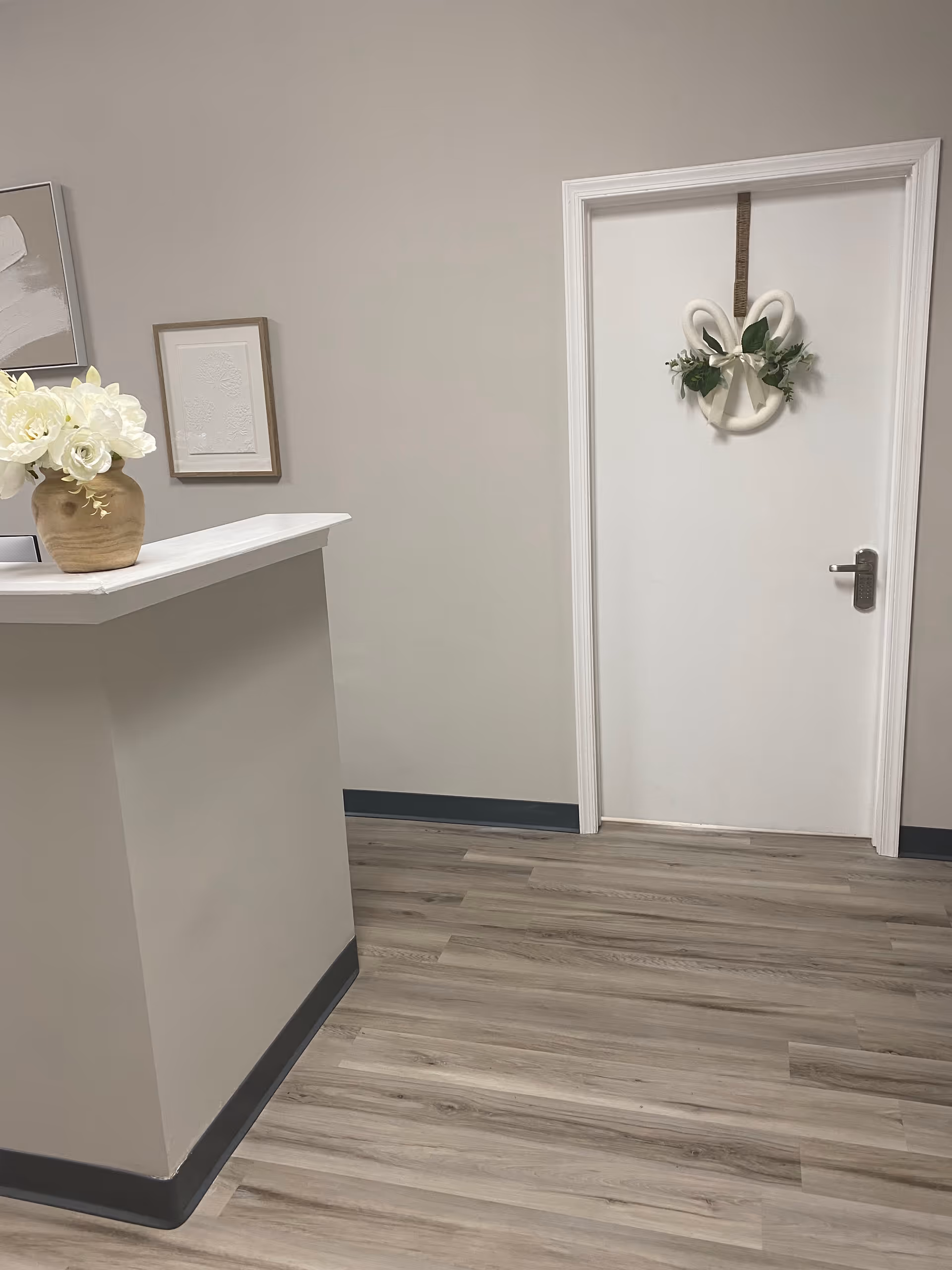 Reception desk in a neutral-toned hallway with a white door adorned by a wreath.