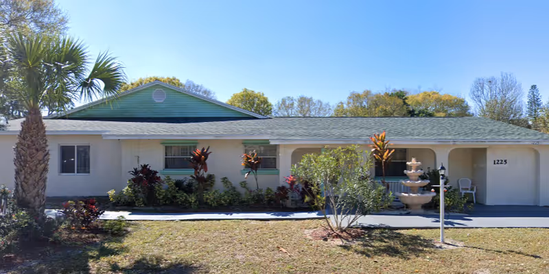 Front exterior of a single-story assisted living building with a small tiered fountain, shrubs, and the address number 1225.
