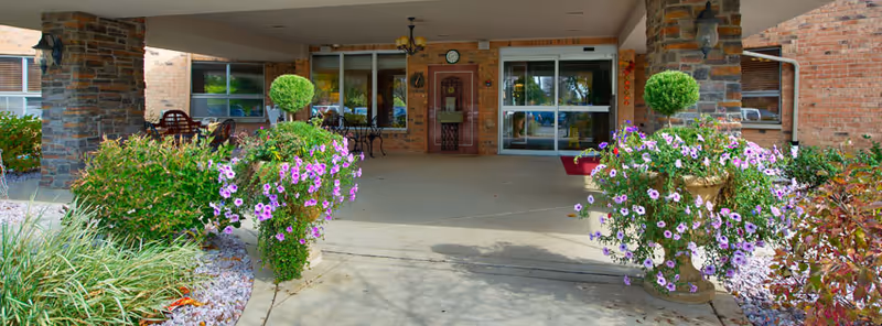 Entrance to Burgess Square Healthcare & Rehab Centre with brick exterior and blooming planters.