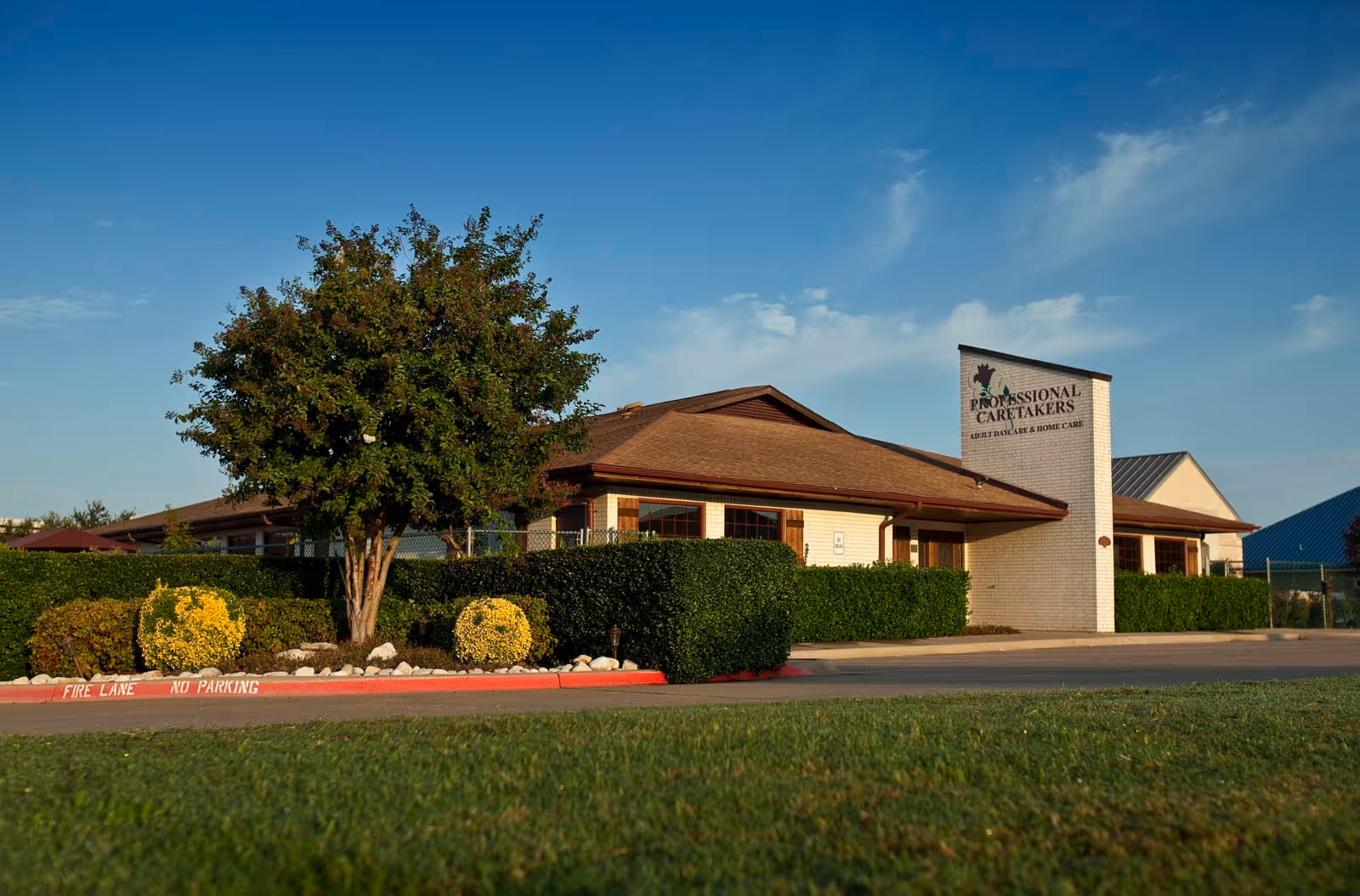Exterior view of a senior care facility with shrubbery and a front entrance sign.