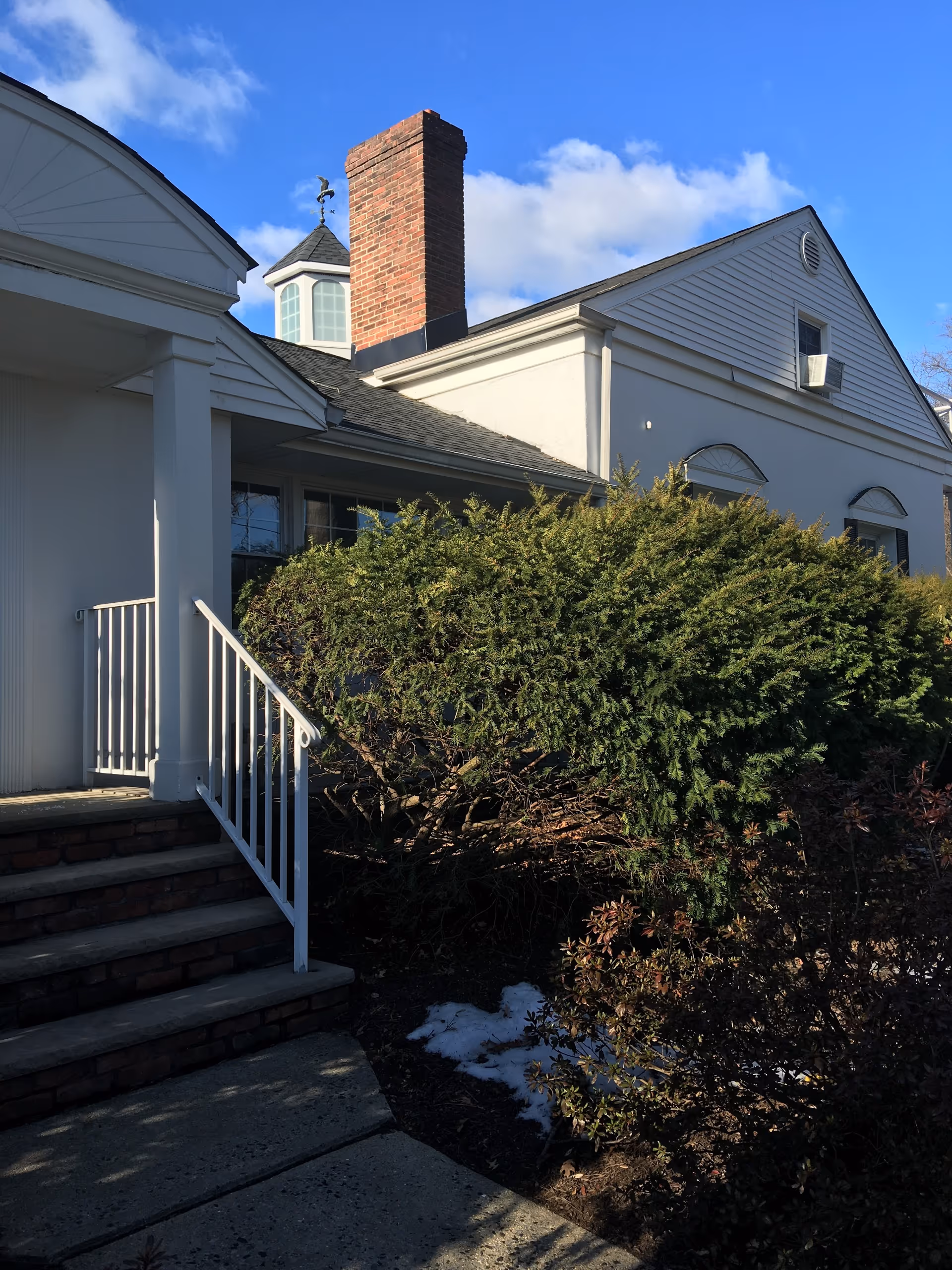 Exterior view of BONJOUR senior living building with stairs, railing, shrubs, and blue sky.