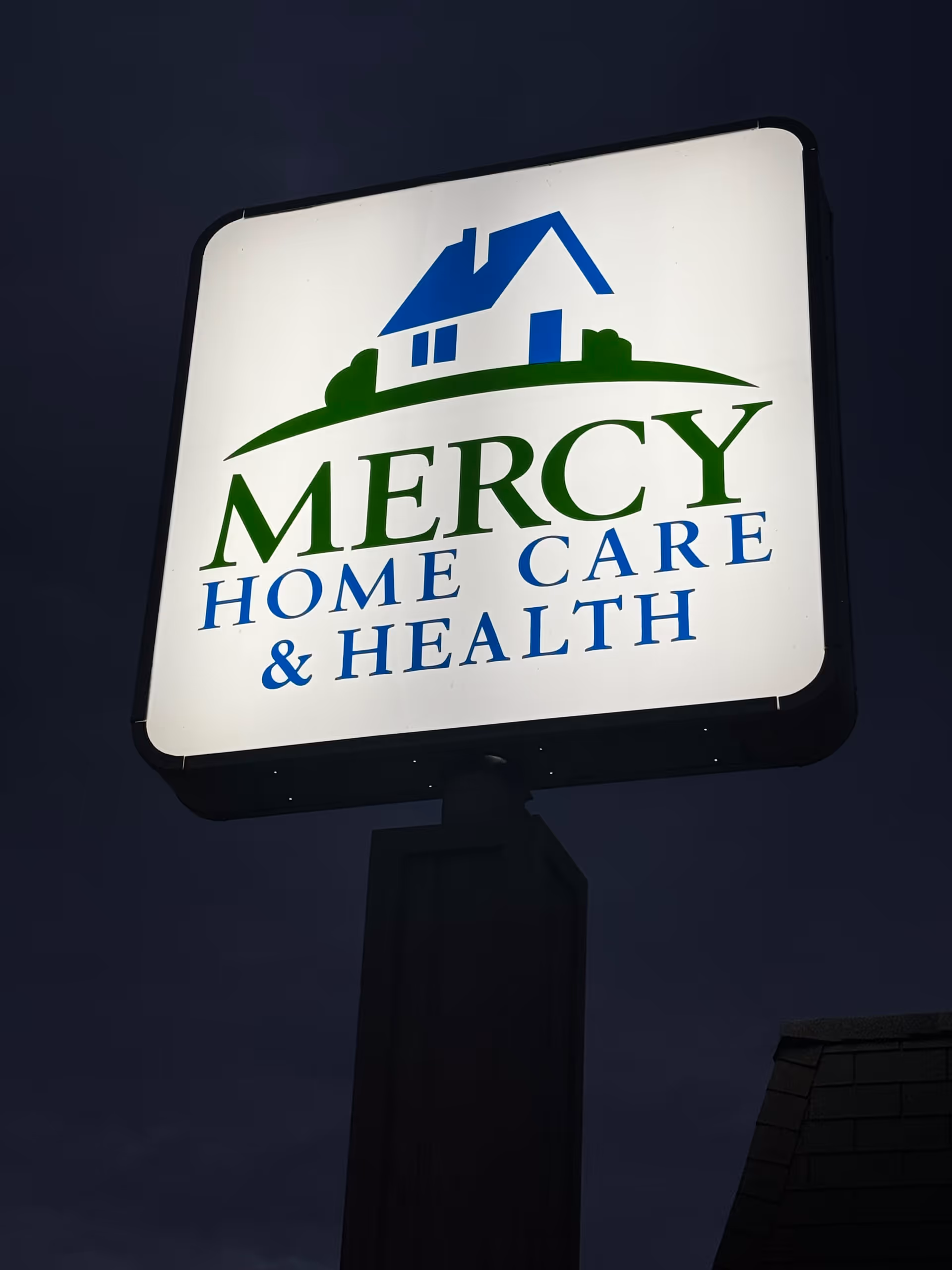 Illuminated Mercy Home Care & Health sign on a tall post outdoors.