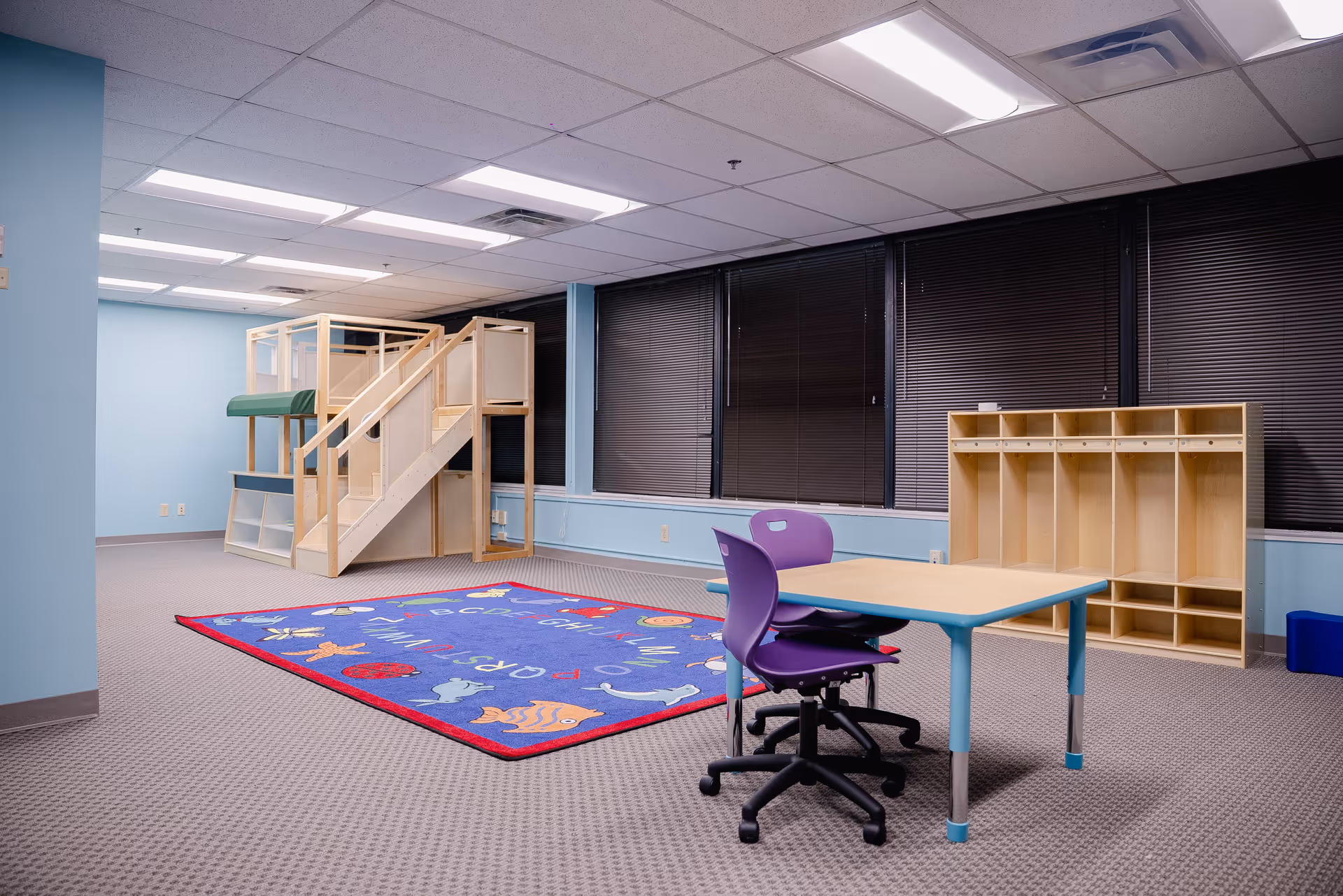 Interior playroom featuring a wooden loft, colorful rug, and a small table.
