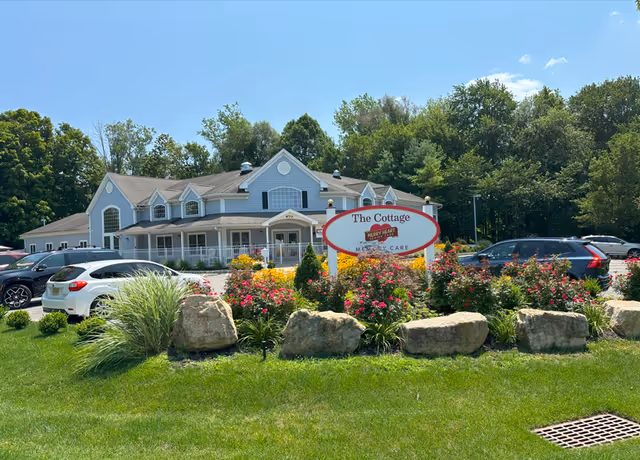 Front view of a light blue senior living building with a landscaped garden and sign.