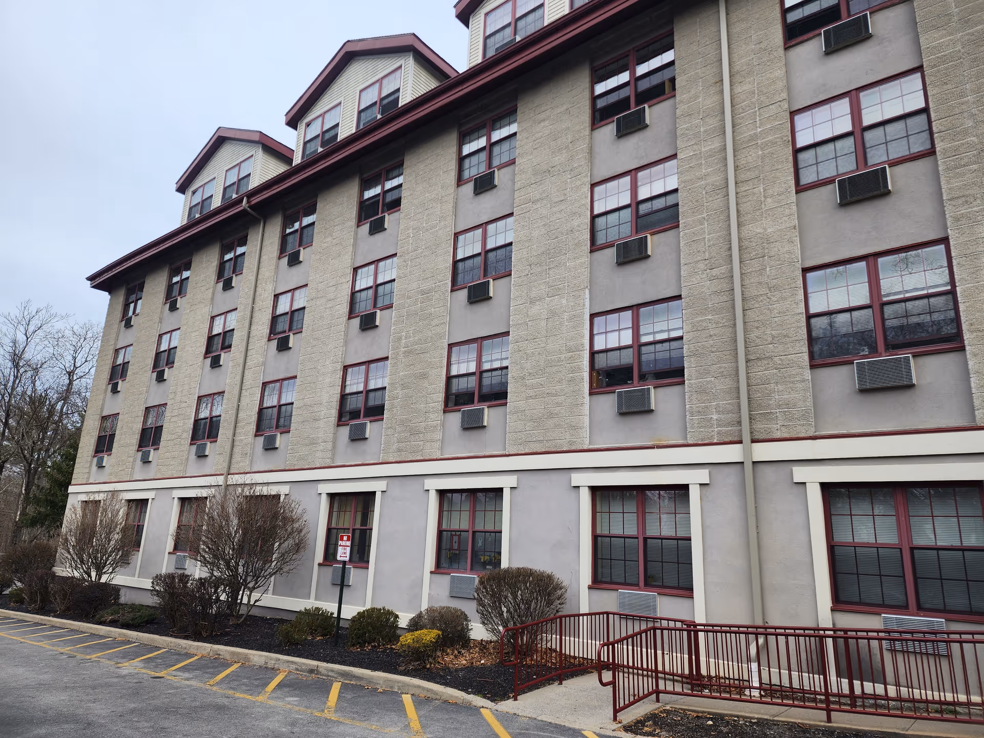 Tall beige senior living building with red-framed windows and visible window AC units.