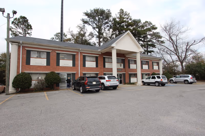 Two-story brick senior living facility exterior with columns and a parking lot.