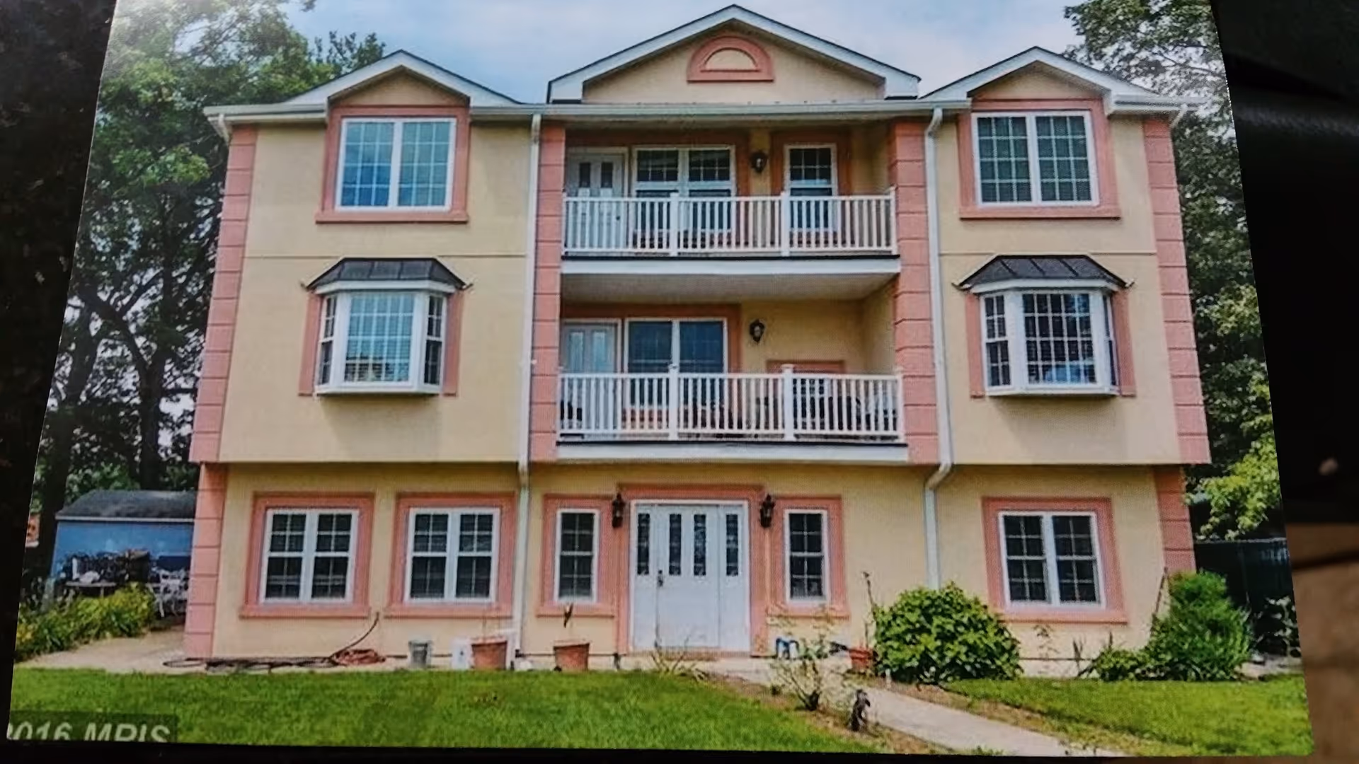 Three-story beige and pink assisted living building with balconies and a grassy front yard.
