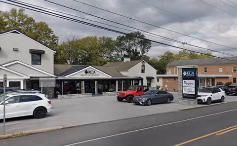 Exterior view of a strip mall with multiple storefronts and parked cars.