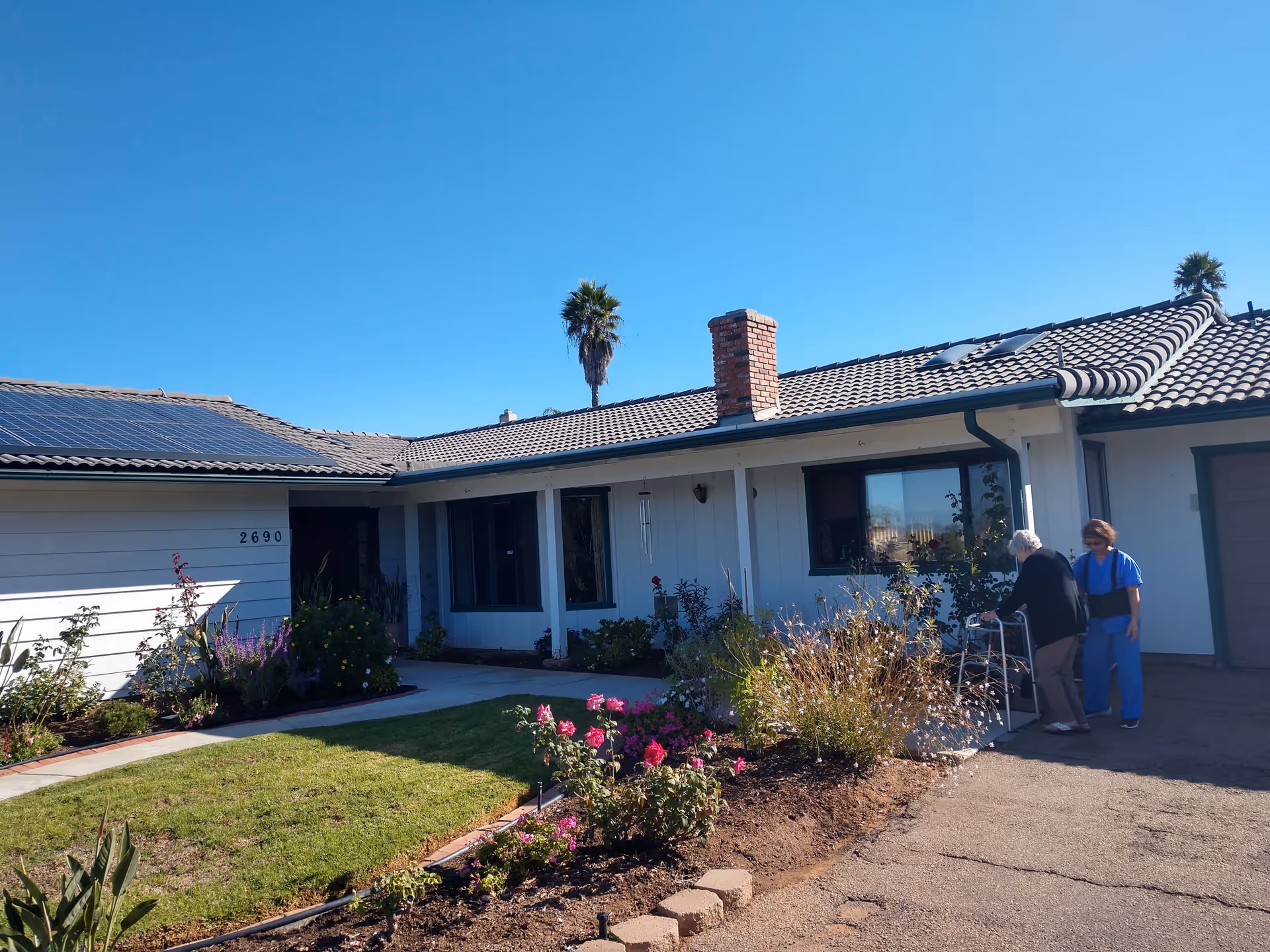 Front view of Anne's Place Assisted Living with landscaped yard and two people at entrance.