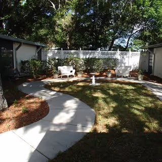 Outdoor courtyard with curved sidewalk, white chairs, potted plants, and a small fountain.