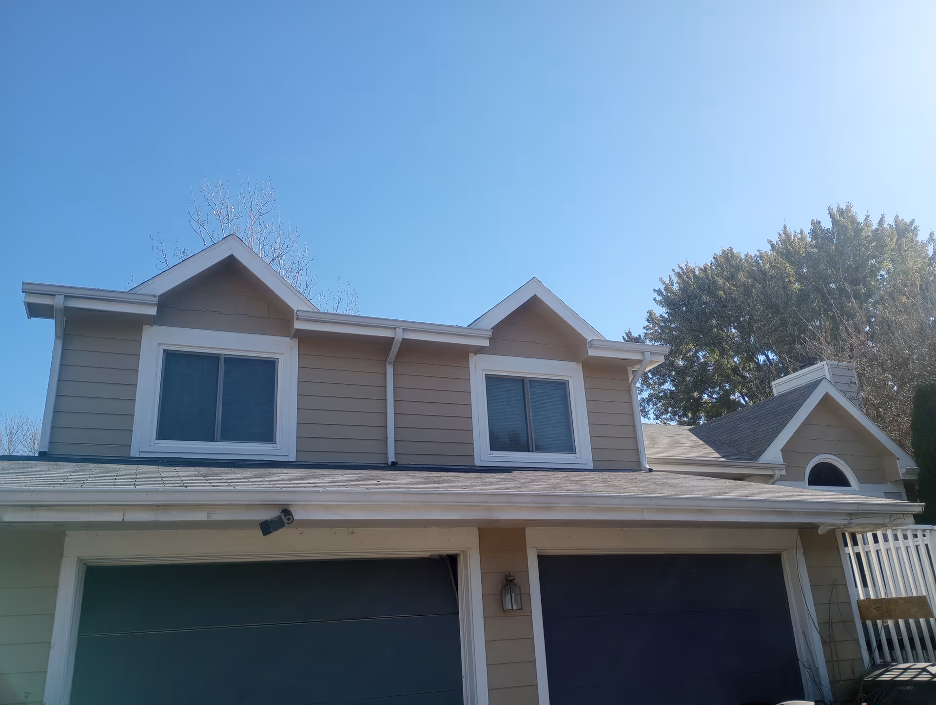 A residential building with two garage doors and dormer windows under a clear blue sky.