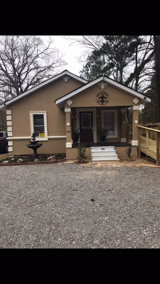 Small beige building with a front porch, columns, and steps.
