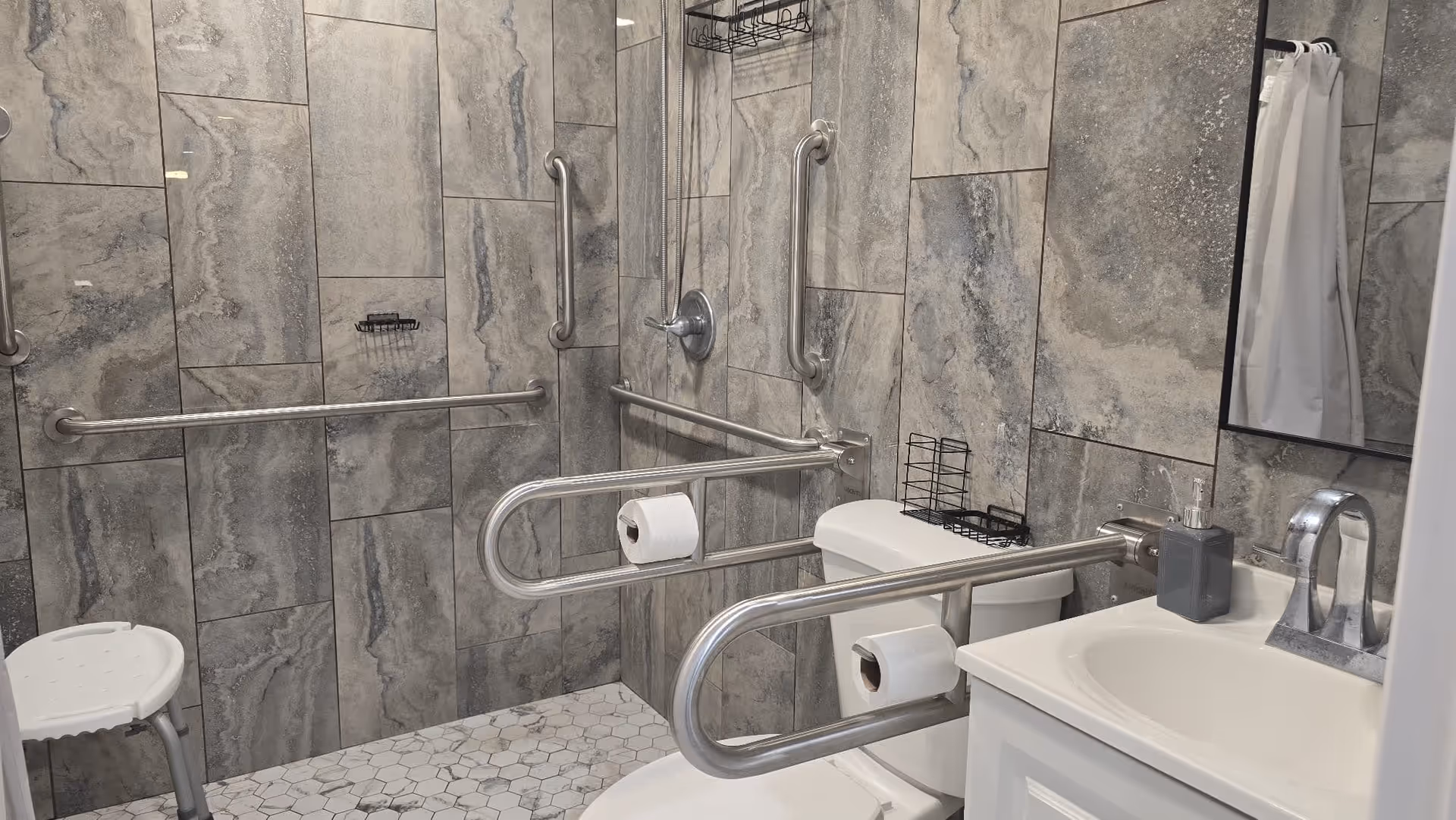 Accessible bathroom with grab bars, tiled walls, a toilet, sink, and mirror.
