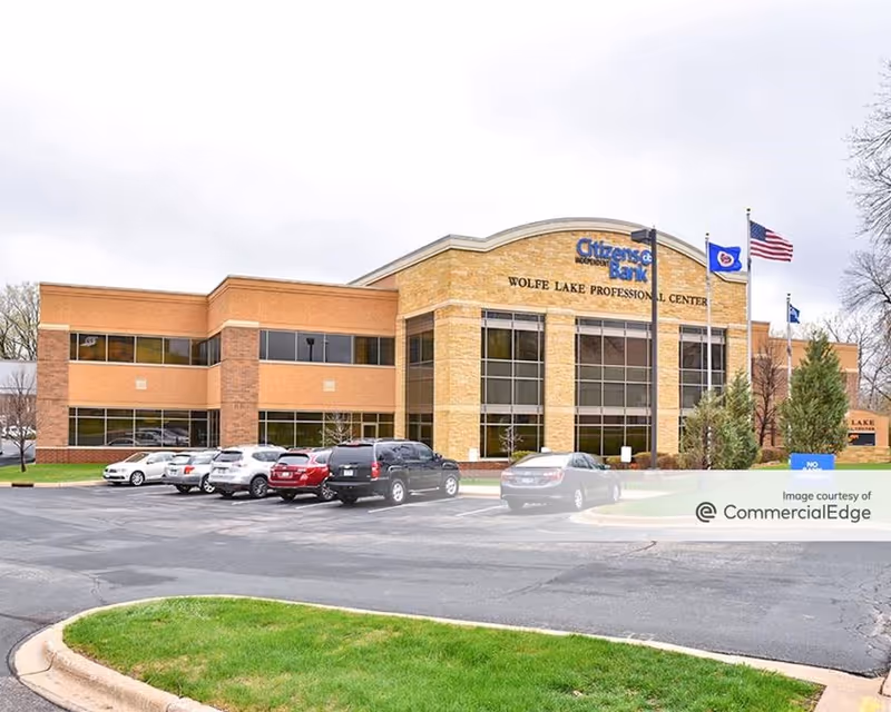 Exterior view of a brick commercial building with a large glass facade and a parking lot.