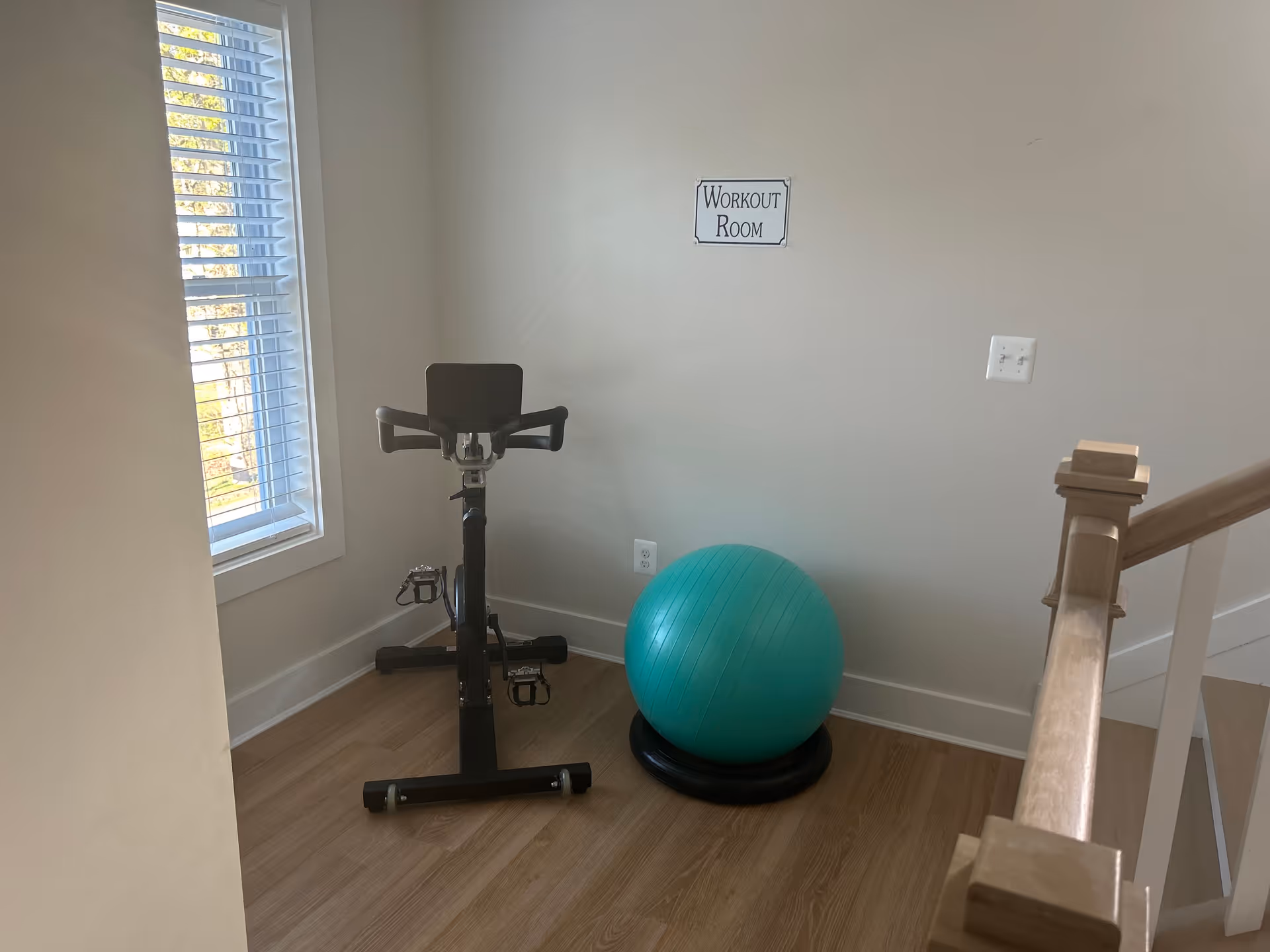 Small interior workout room with a stationary bike, exercise ball, and a Workout Room sign.