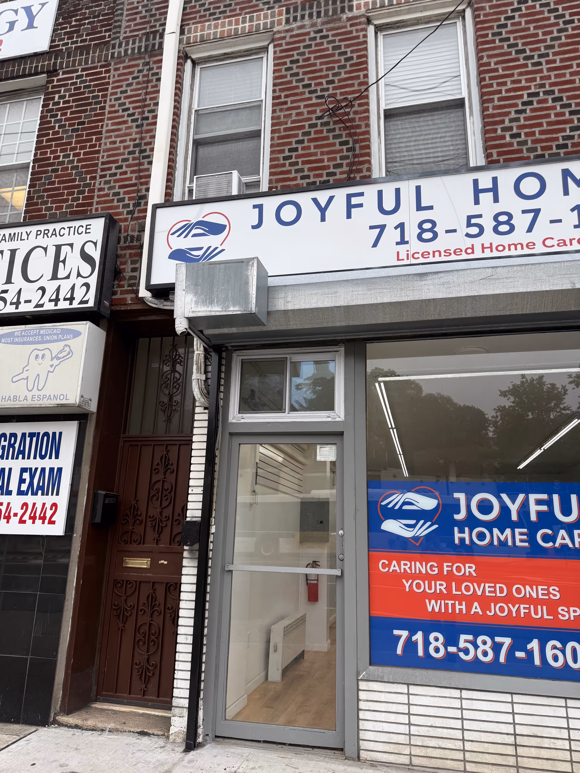 Brick storefront with Joyful Home Care sign, glass door, and banners outside.