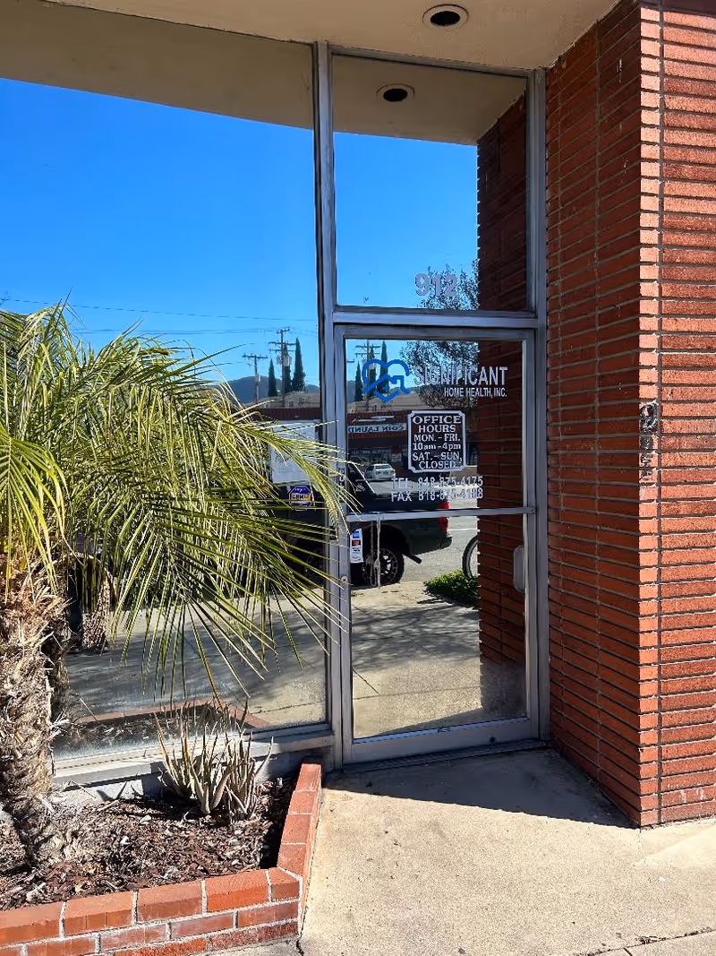 Exterior storefront with glass door, brick wall, and a plant planter outside.