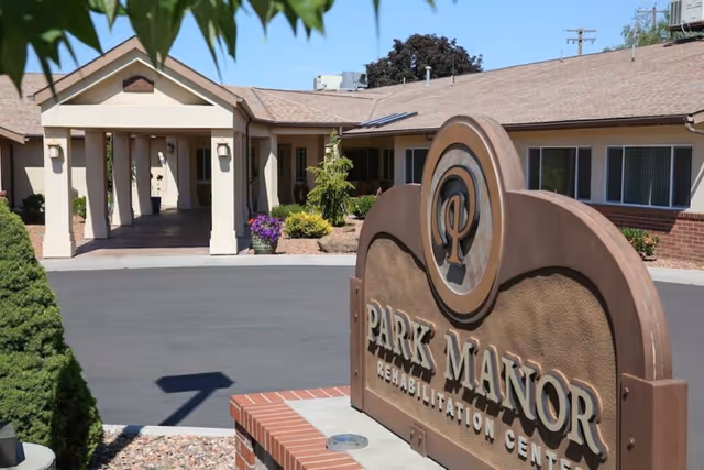 Entrance of Park Manor Rehabilitation Center with a large sign in the foreground and the building entrance and portico in the background.