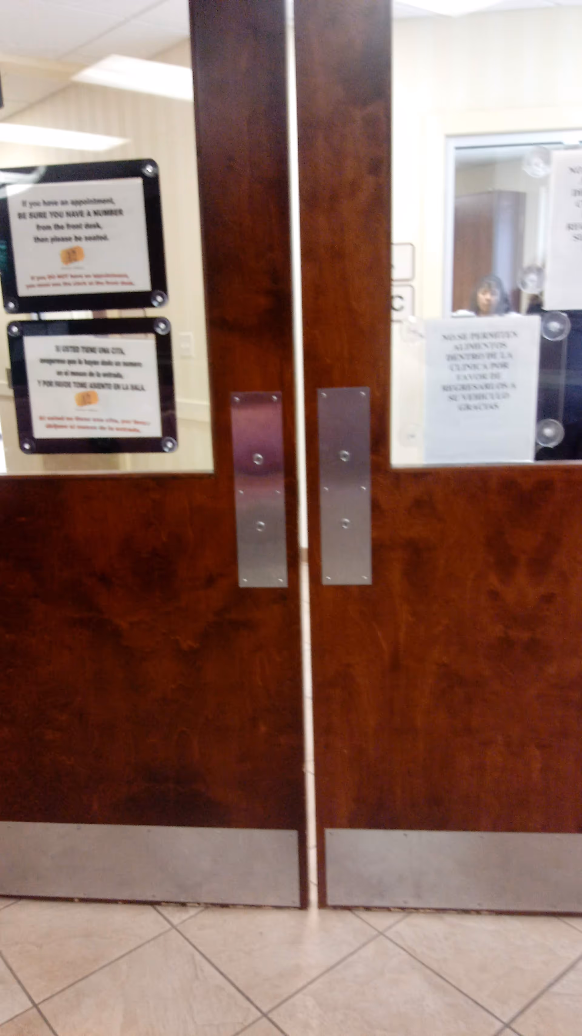 Double wooden doors with metal handles and posted notices inside a facility corridor.