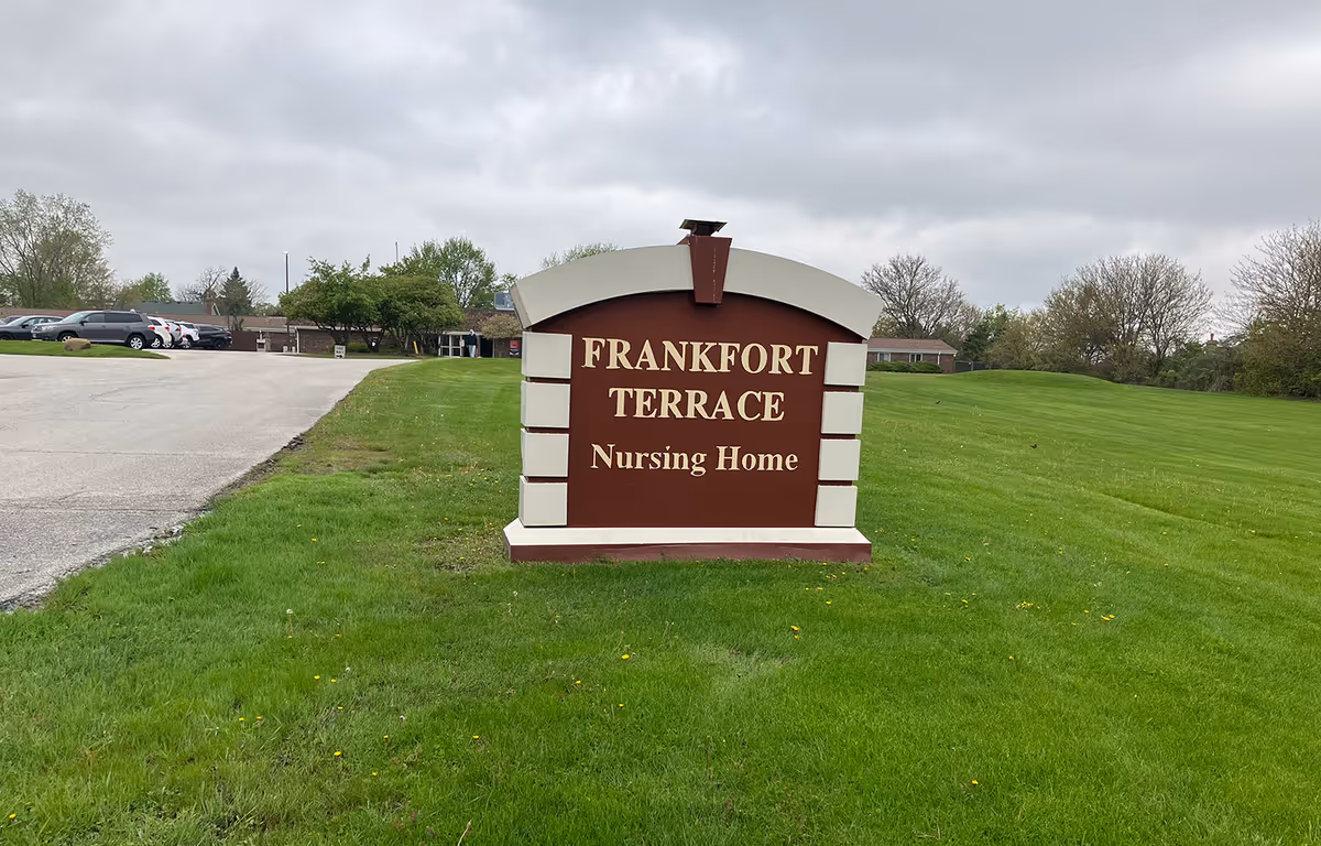 A freestanding sign reading 'Frankfort Terrace Nursing Home' on a grassy lawn with the facility and parking lot in the background.