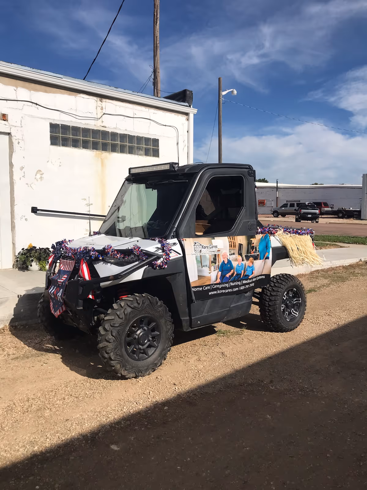 A decorated utility vehicle with Kore Cares banners parked outside a white building.