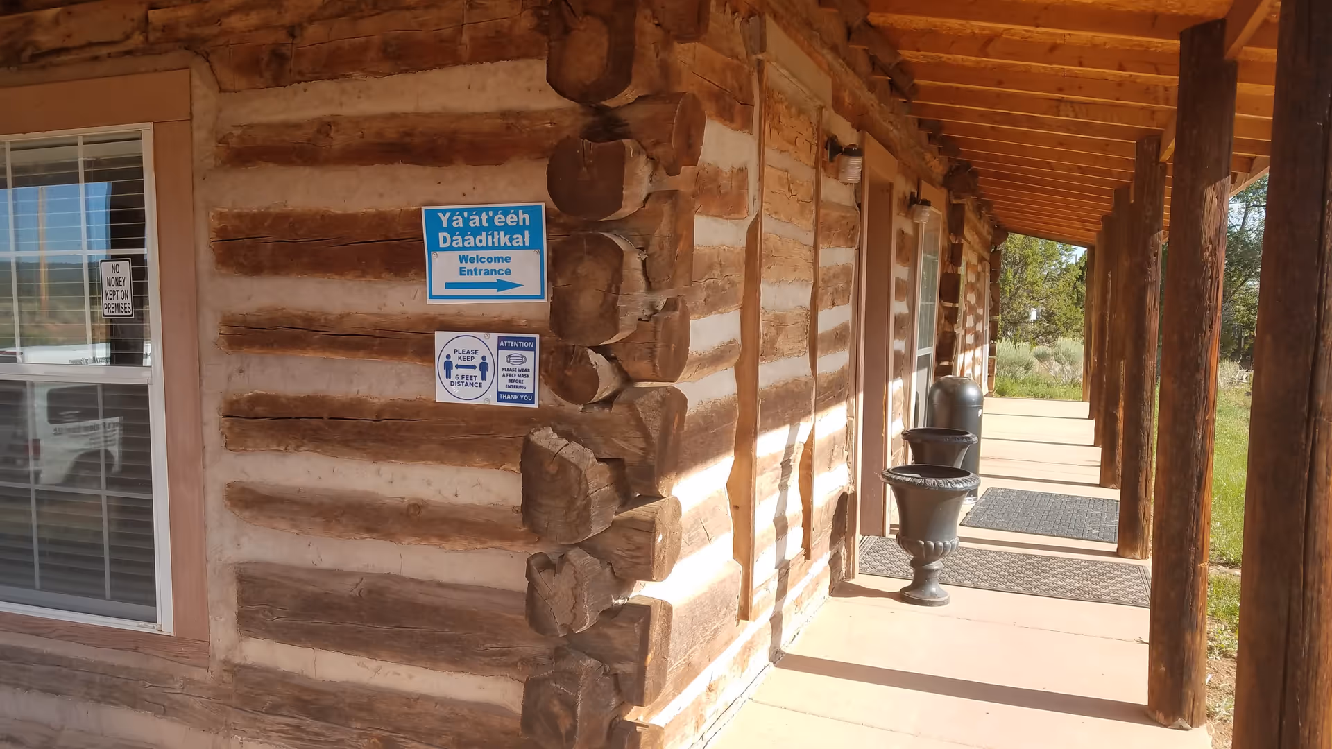 Log cabin exterior with a covered walkway, wooden posts, and blue signs near a glass door.